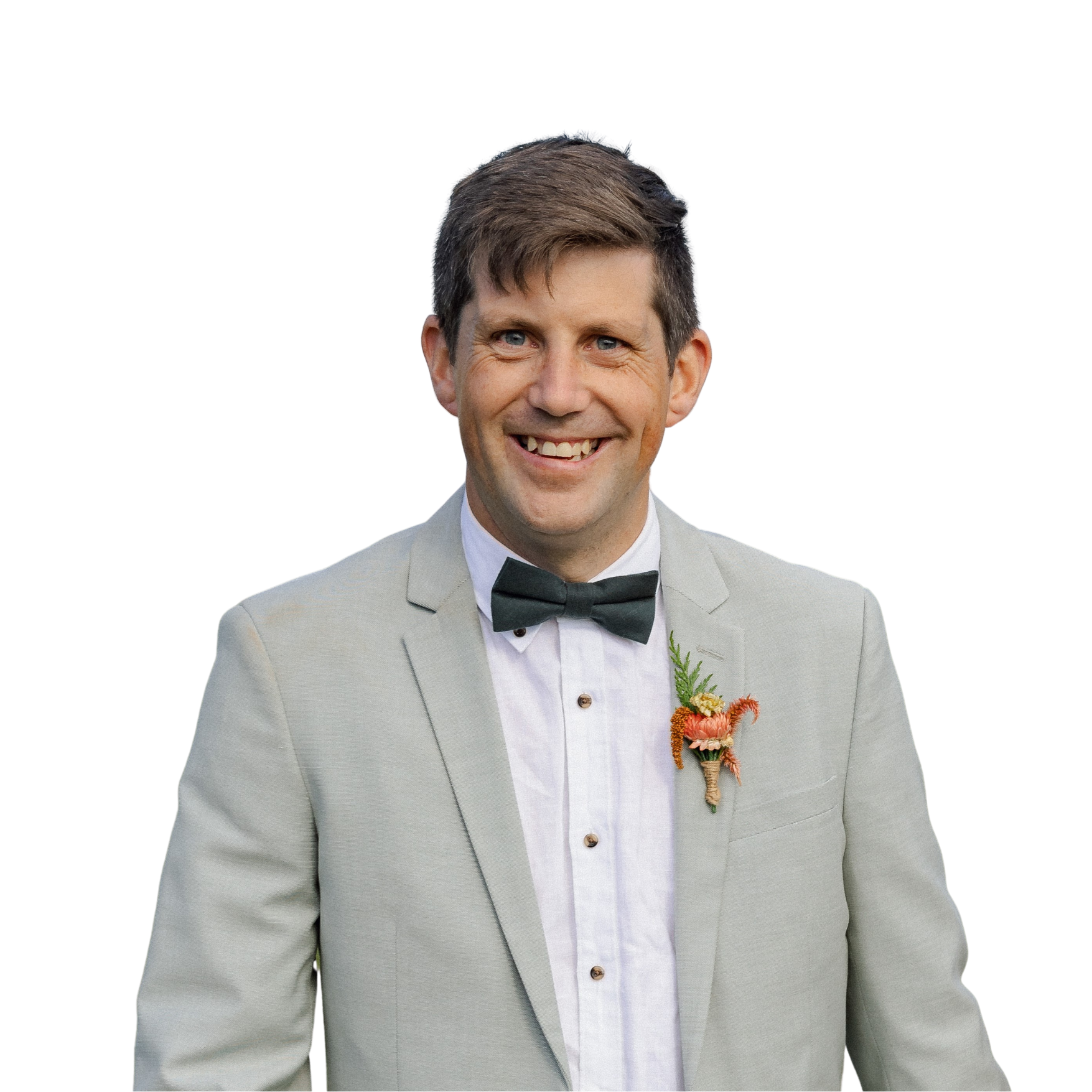 A man in a light gray suit with a black bow tie, white shirt, and a boutonniere, smiling at the camera, against a white background.