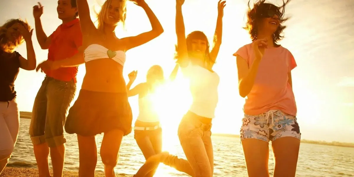 Group of young women and girls joyfully dancing and running on a beach during sunset.