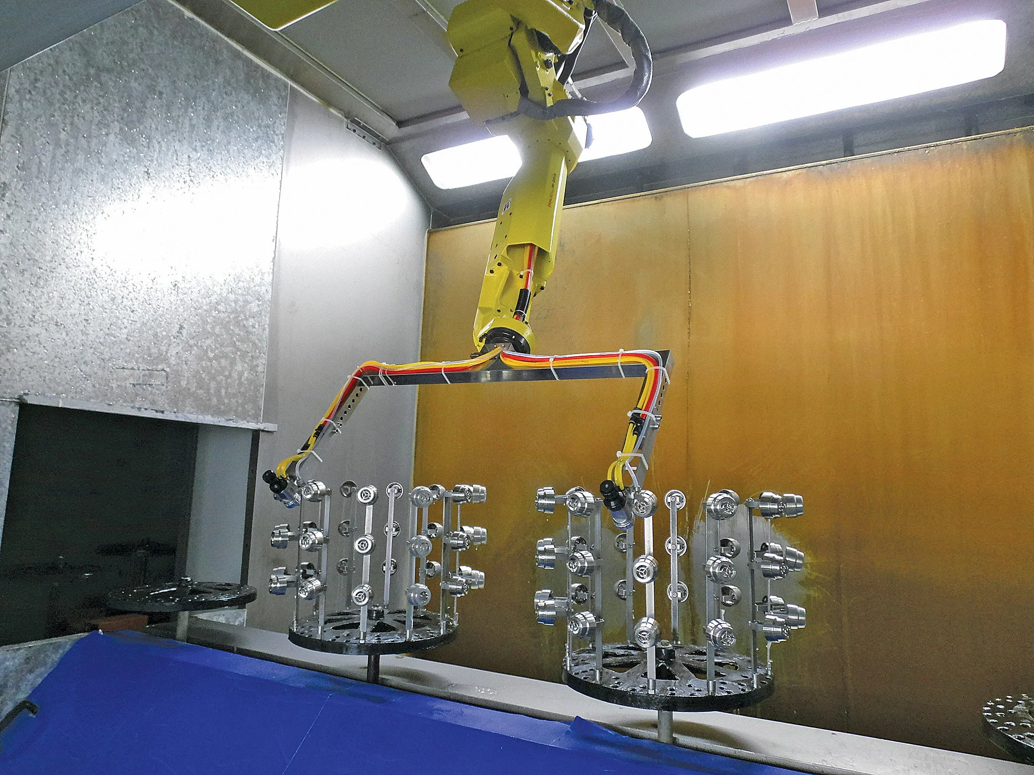 Spray painting automation machine, spraying color and optimizing the surface finsih of showerheads. A robotic arm performing an automated task with metallic fixtures on a manufacturing or assembly line in a controlled environment.