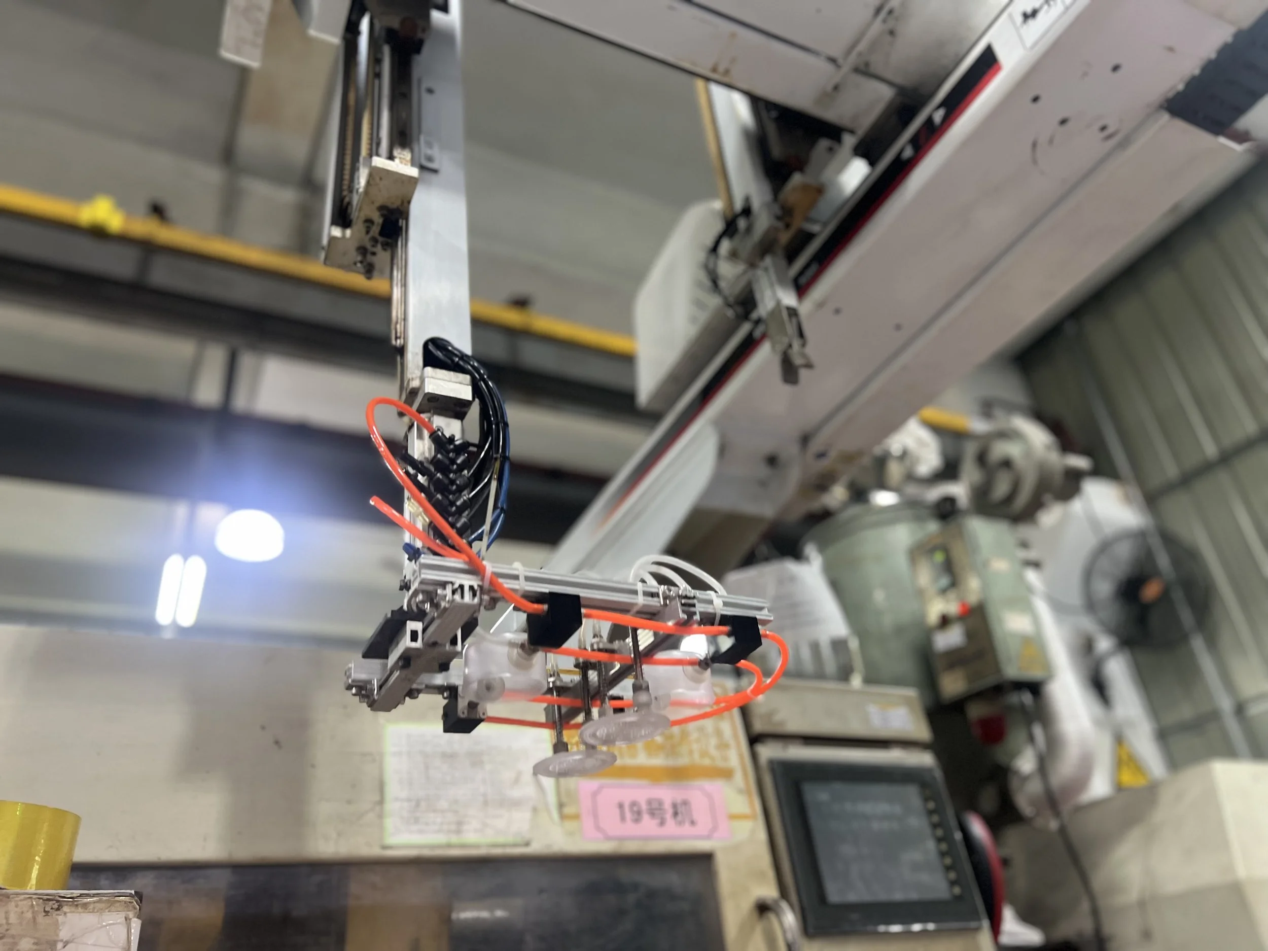 Close-up of a robotic arm with wires and mechanical components, suspended in a laboratory or manufacturing environment with industrial equipment in the background.