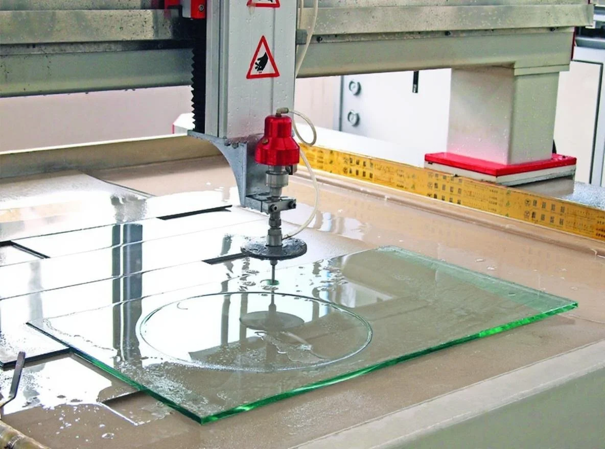 A glass sheet is being cut with a water jet cutting machine in a workshop.