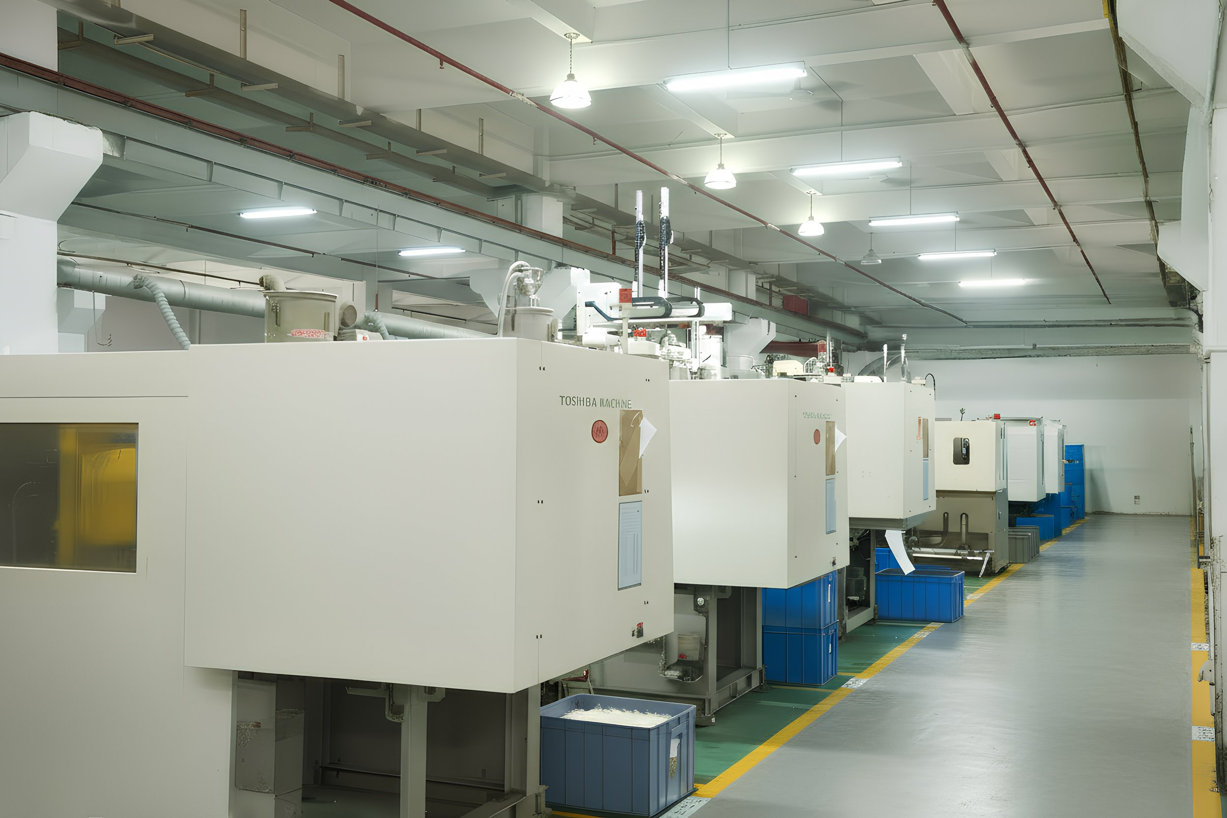 Industrial facility with multiple large white machines, pipes, and blue containers in a well-lit, clean environment.