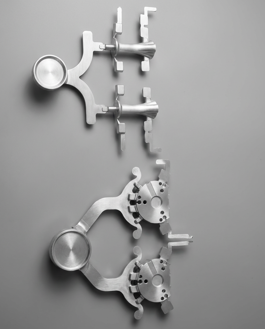 Two set of metallic surgical instrument parts, symmetrical, arranged against a plain gray background.