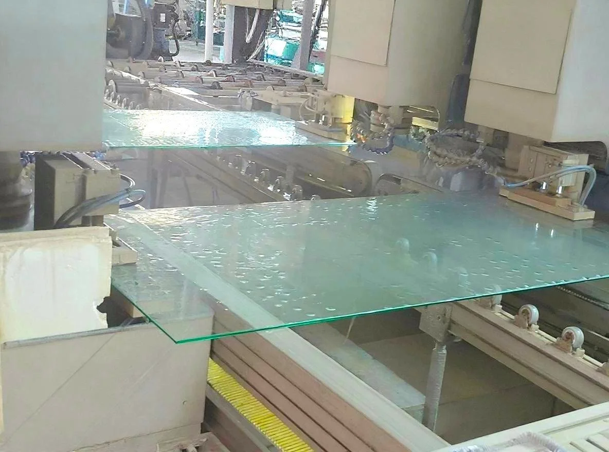 Manufacturing process involving a glass sheet moving through machinery, with water or lubrication on the glass surface.