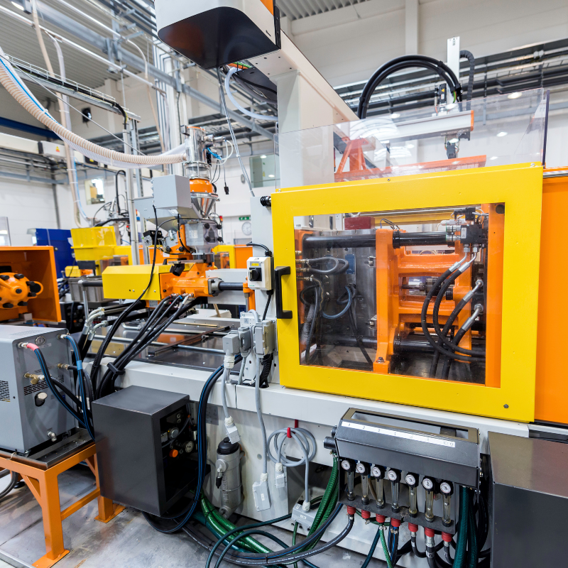 Industrial manufacturing machinery with yellow safety enclosure, wires, and control panels in a factory setting.