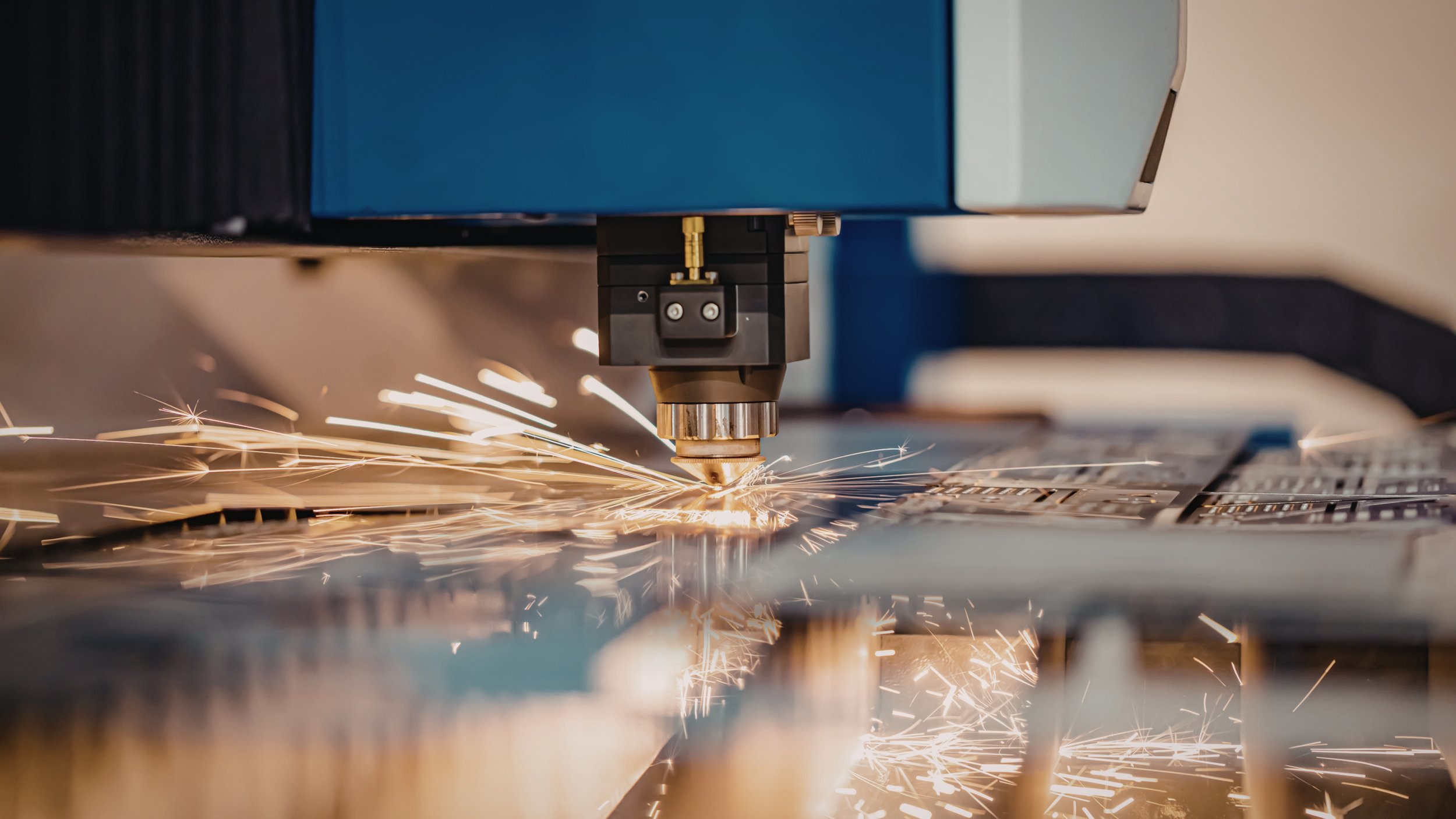 A close-up of a laser cutting machine in operation, cutting through sheet metal, with sparks flying.