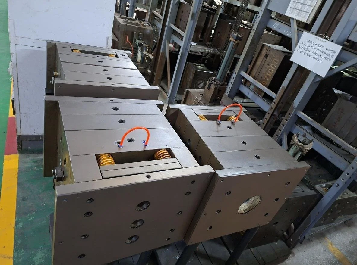 Metal molds or parts with hydraulic or pneumatic fittings on a workbench in an industrial or manufacturing setting. Tooling and mold fabrication for injection molding, producing showerheads