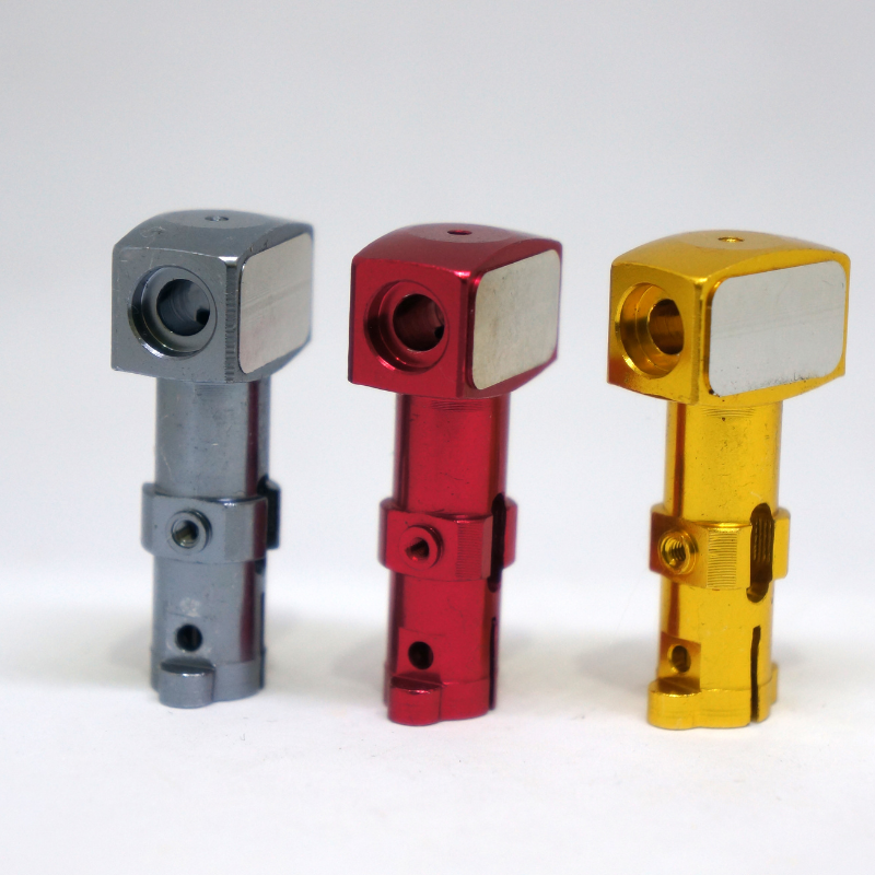 Three metal hose fittings in silver, red, and gold colors standing on a white surface.