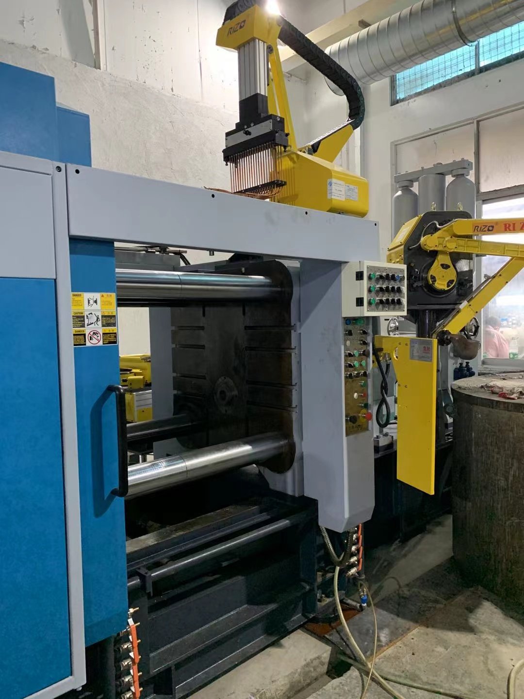 Industrial manufacturing machine with yellow robotic arm and control panel, situated in a factory setting.