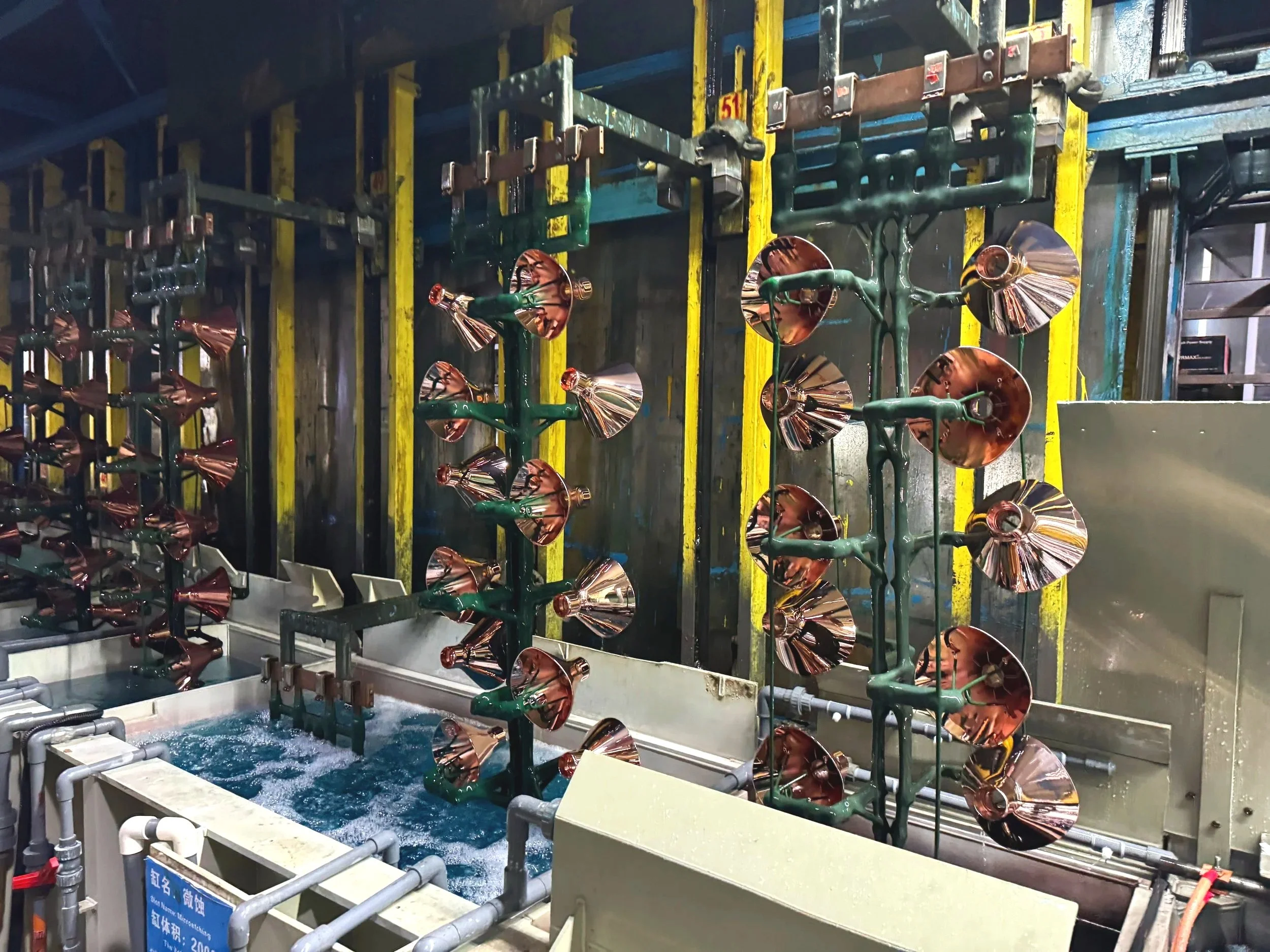 Performing the process of electroplating, Multiple industrial lamps on green metal frames surrounded by pipes and yellow supports in an industrial setting.