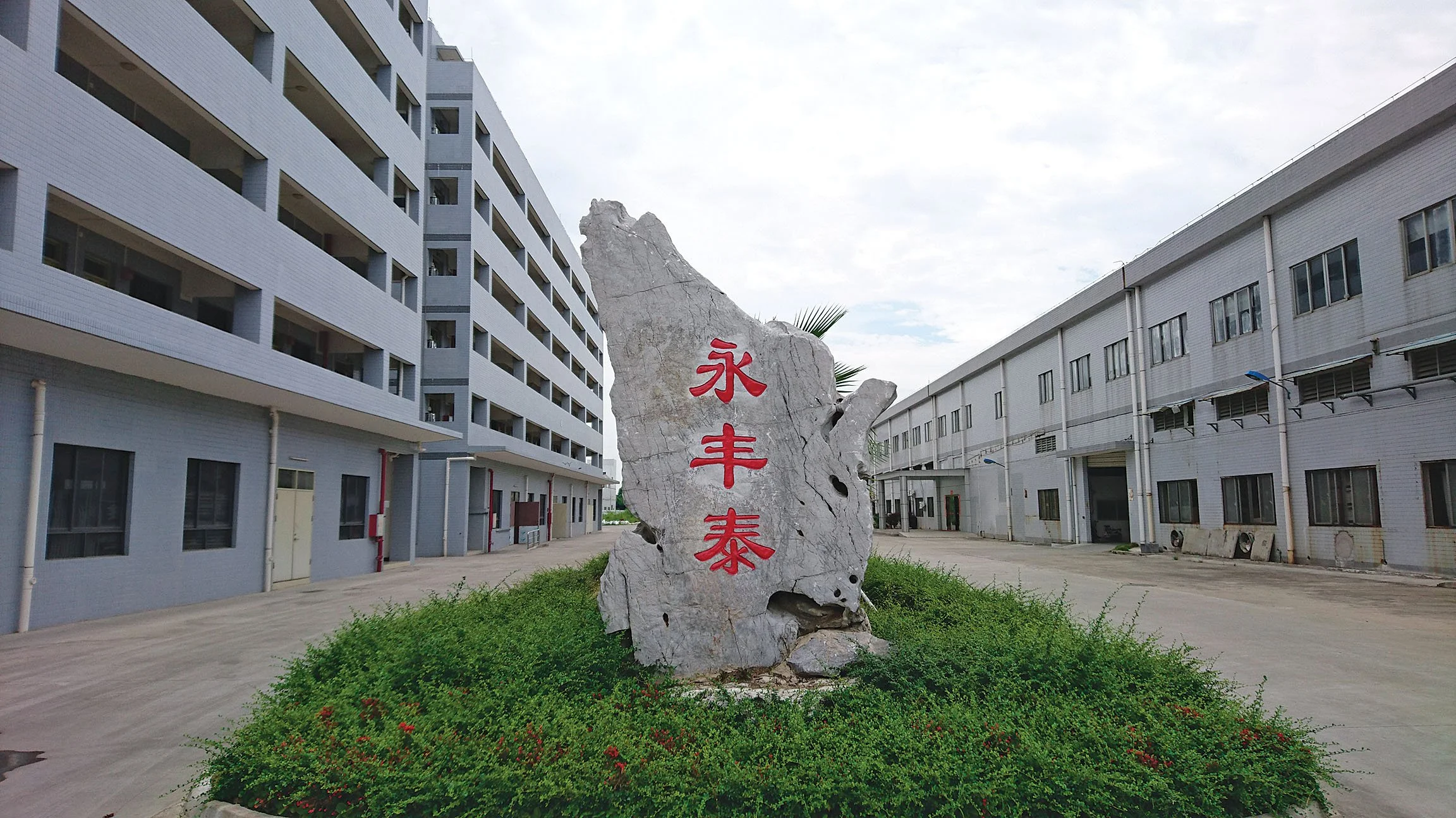 A large stone with red Chinese characters engraved on it, situated on a green grassy area surrounded by modern industrial buildings.