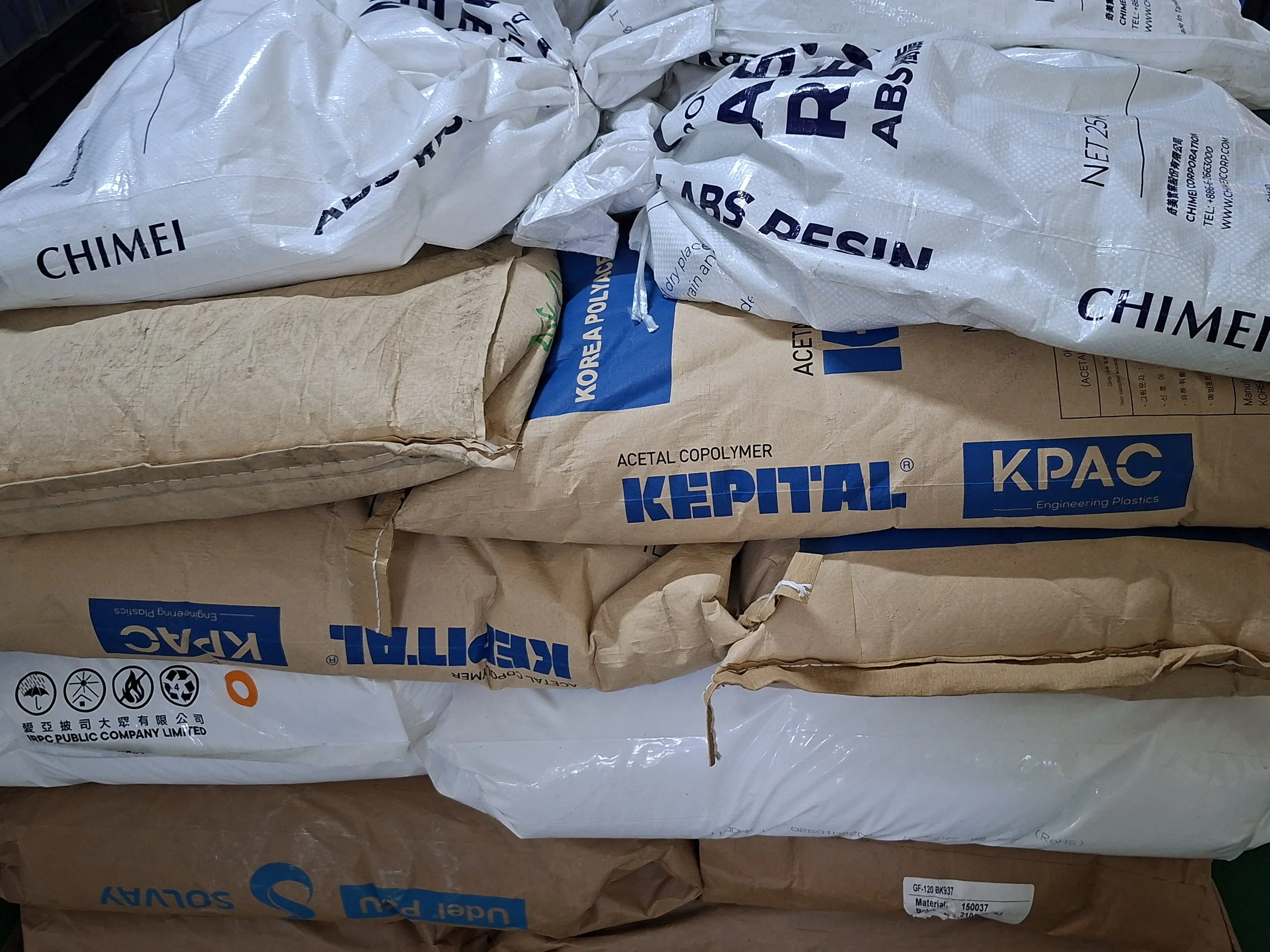 Stacks of plastic and paper bags, some labeled with branding such as Kepital and Korea Polyplast, containing raw materials or chemicals.