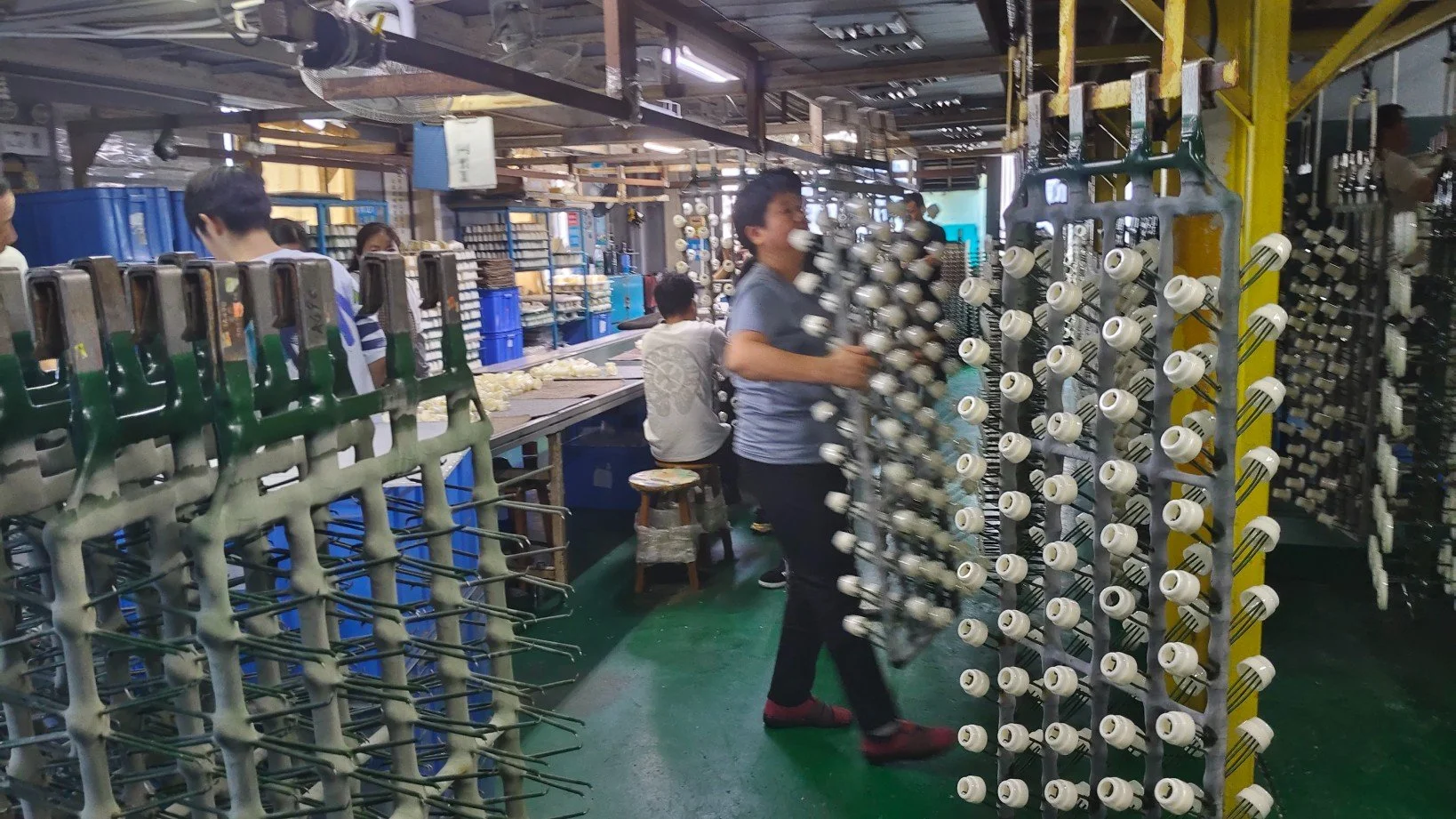 Workers in a factory assembling or handling ceramic or porcelain insulators for electrical equipment. Electroplating process handling by workers