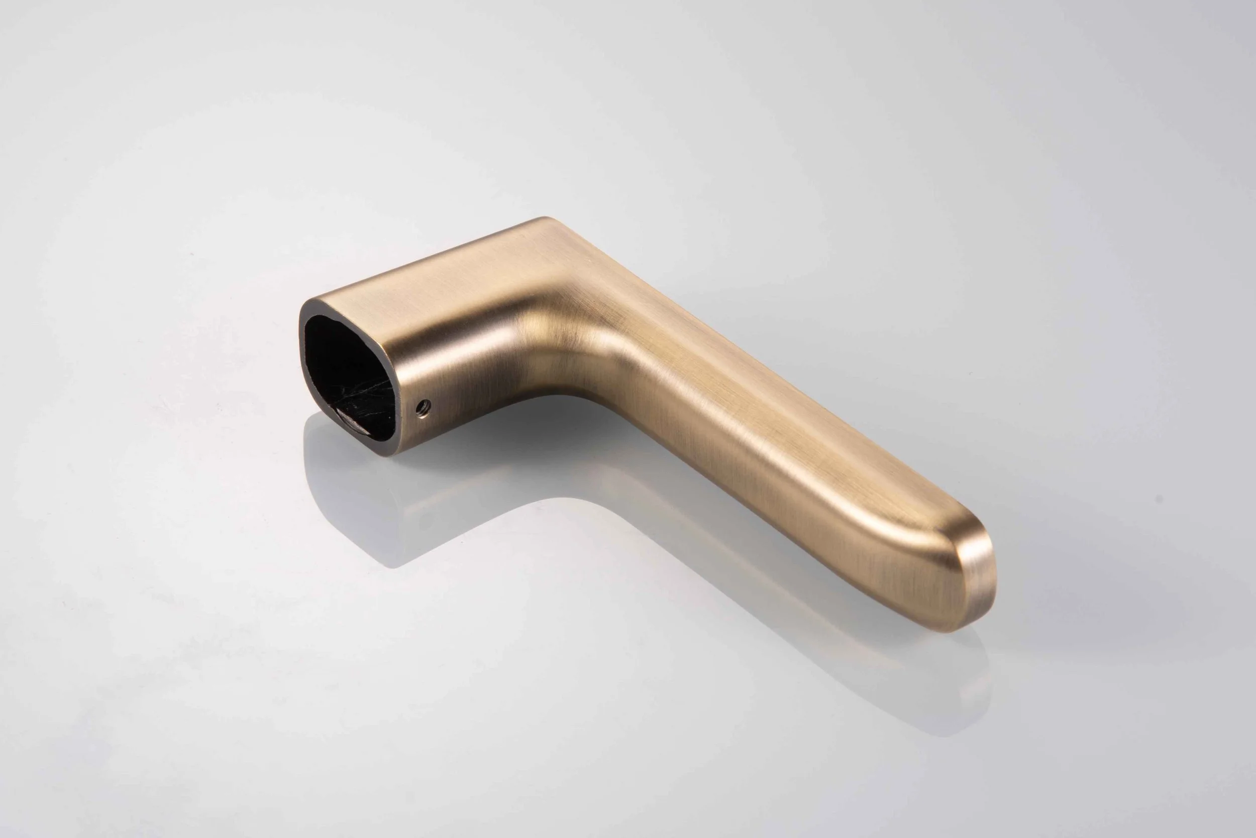 A metallic gold-colored pipe fitting with a 90-degree bend on a white reflective surface.