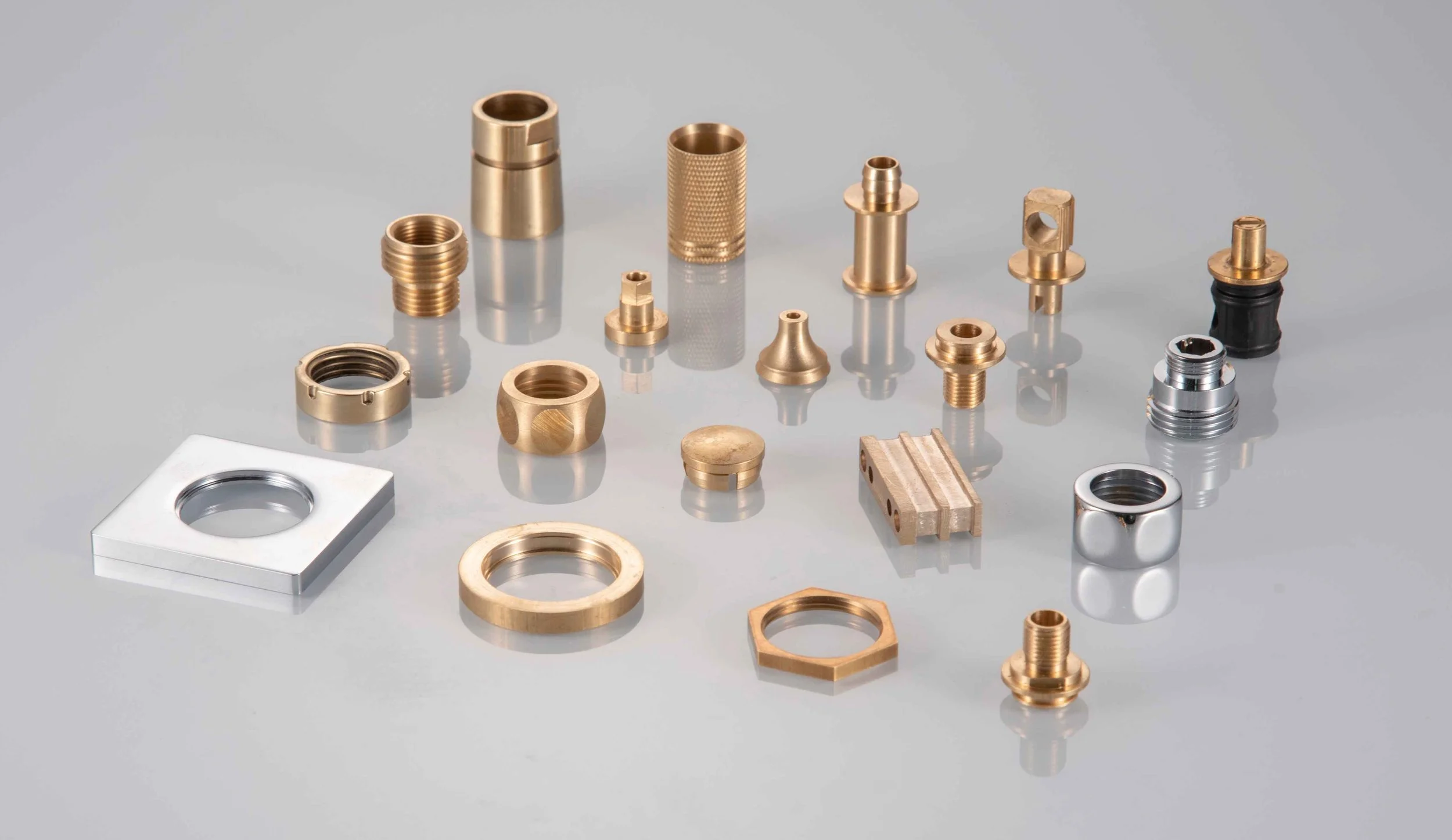 Collection of small metallic parts and fittings, including threaded rings, bushings, and connectors, arranged on a reflective surface.