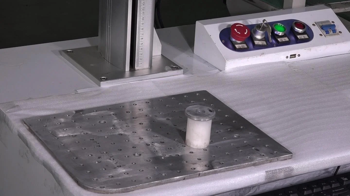 Laboratory equipment with a metal platform, a cylindrical container with a lid, and control buttons including a red emergency stop, a green start button, and other controls on a work surface.