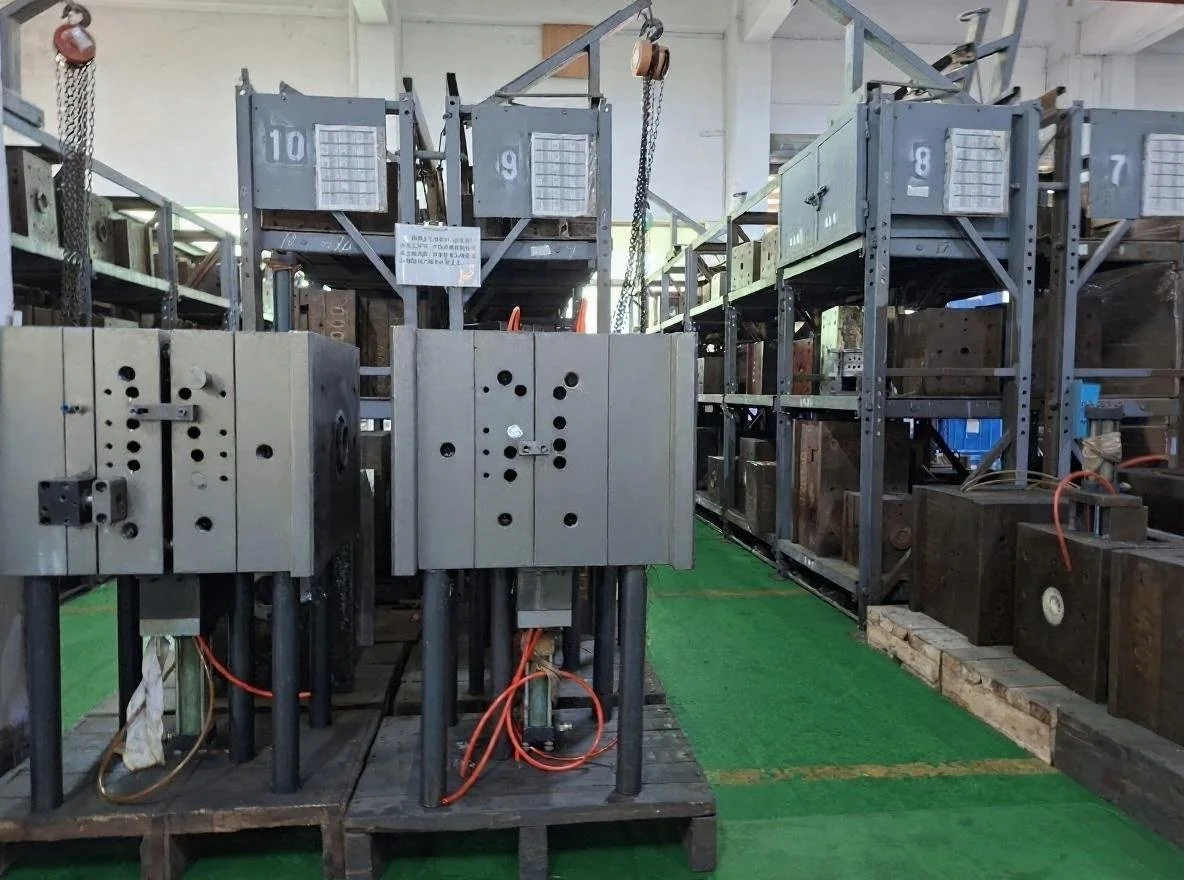 Industrial molds and machinery arranged on shelves and pallets in a warehouse.