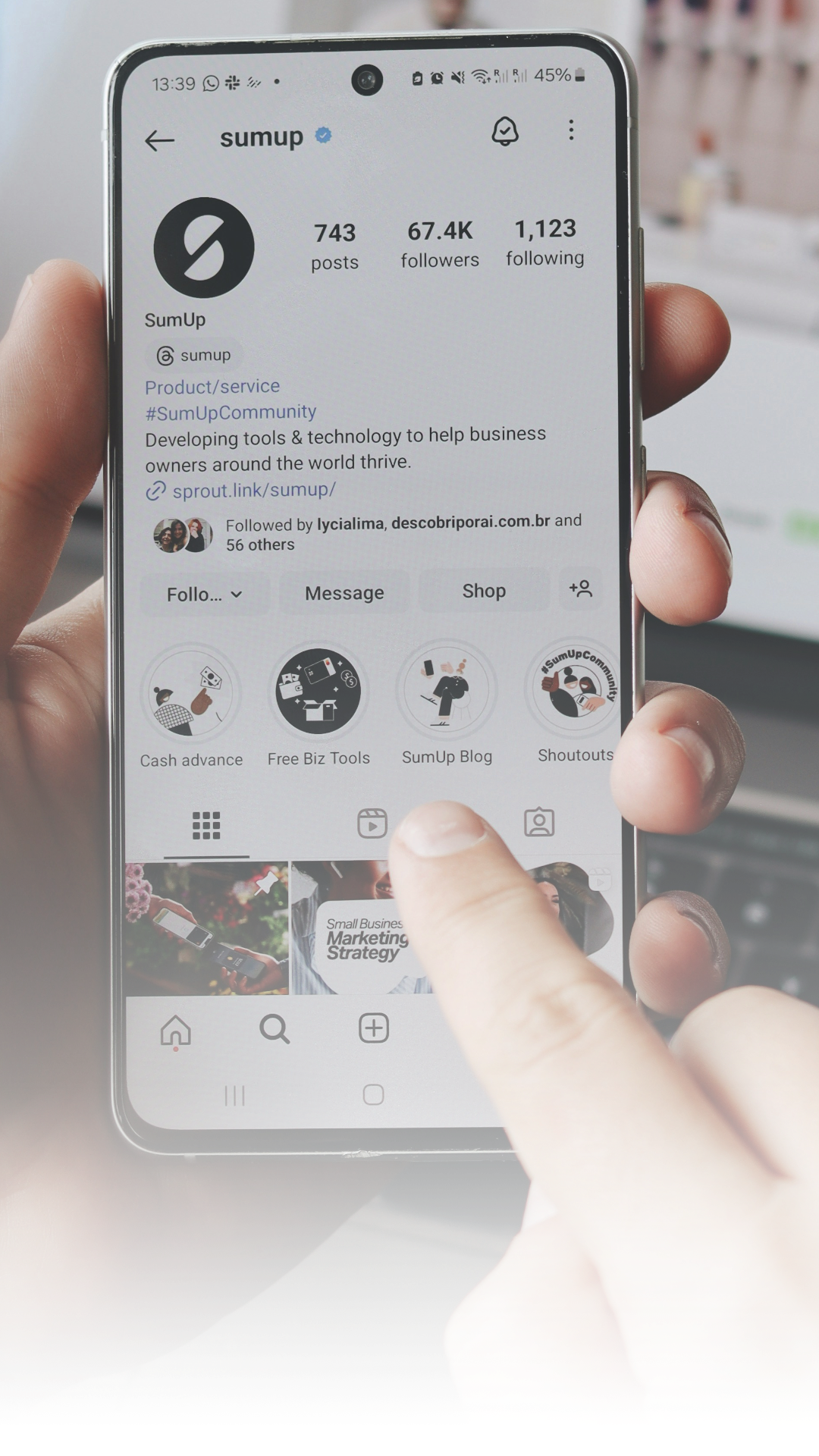 A person holding a smartphone displaying the Instagram profile of 'sumup,' a business account with 743 posts, 67.4K followers, and 1,123 following. The screen shows various story highlight icons and the top part of the phone's interface.