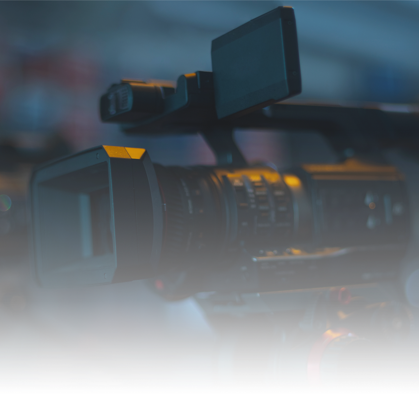 Close-up of a professional video camera on a tripod with a monitor attached, in a dimly lit environment.
