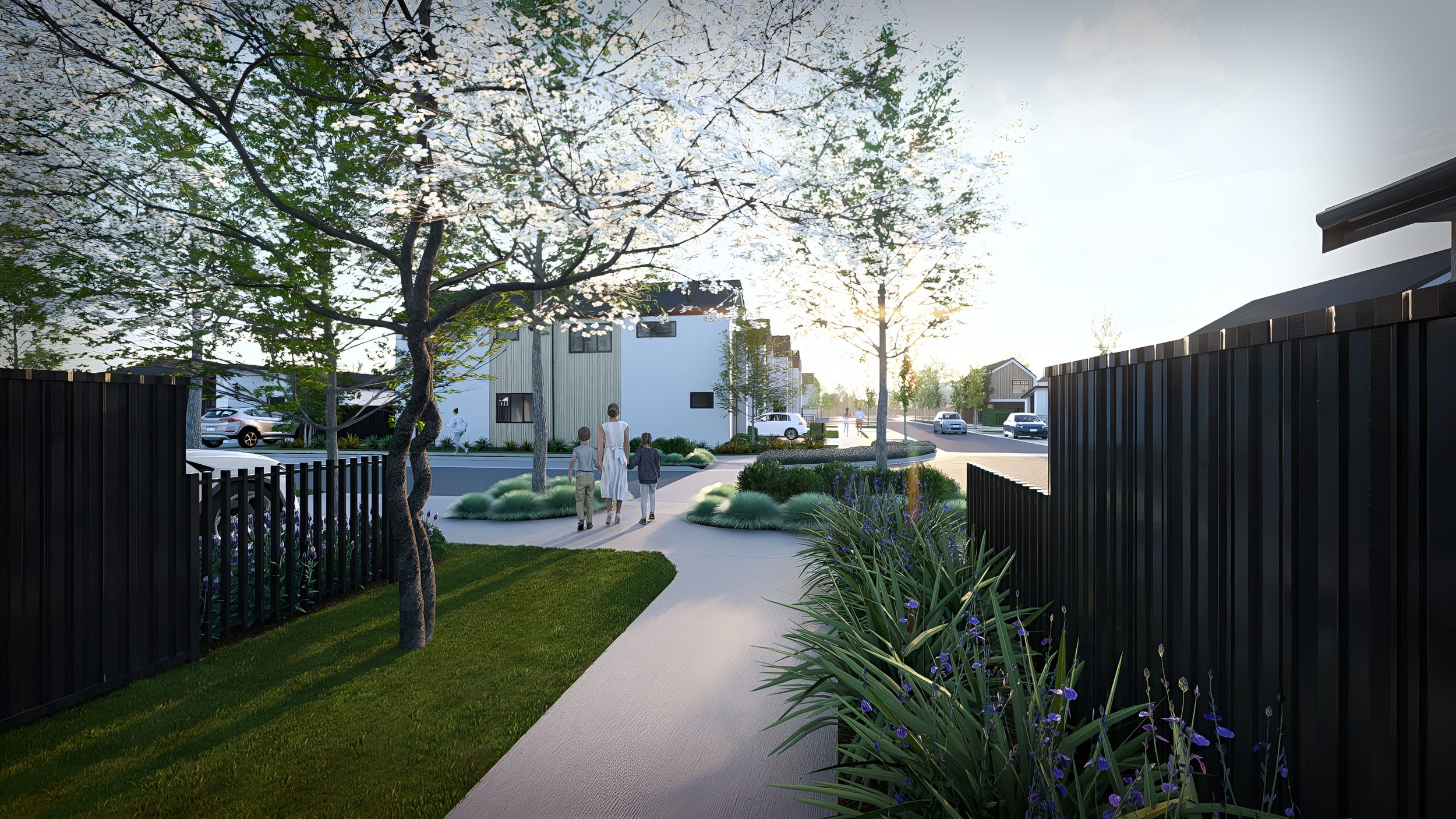 Family walking on a sidewalk in a residential neighborhood during sunset, with modern houses, trees, purple flowers, and a black fence.
