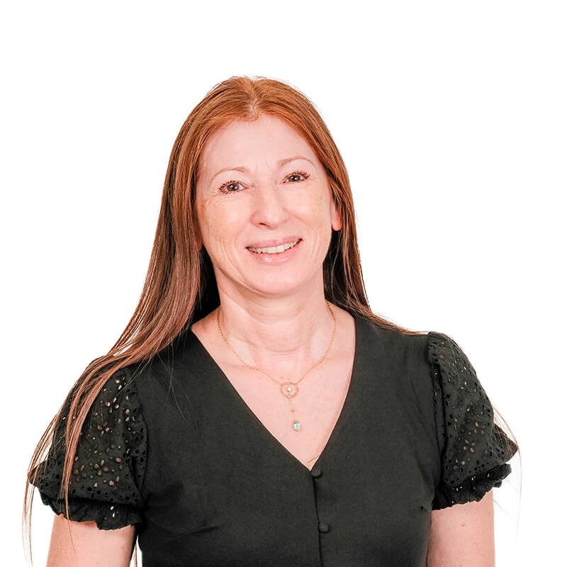 A woman with long red hair, wearing a black top with lace sleeves, and layered necklaces, smiling against a white background.