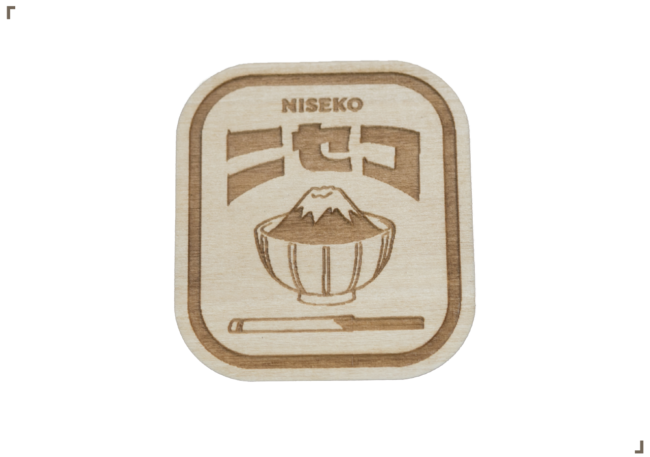 Wooden engraving of a bowl of rice with mountain in the background, the word "NISEKO" and Japanese characters above, and a katana sword at the bottom.