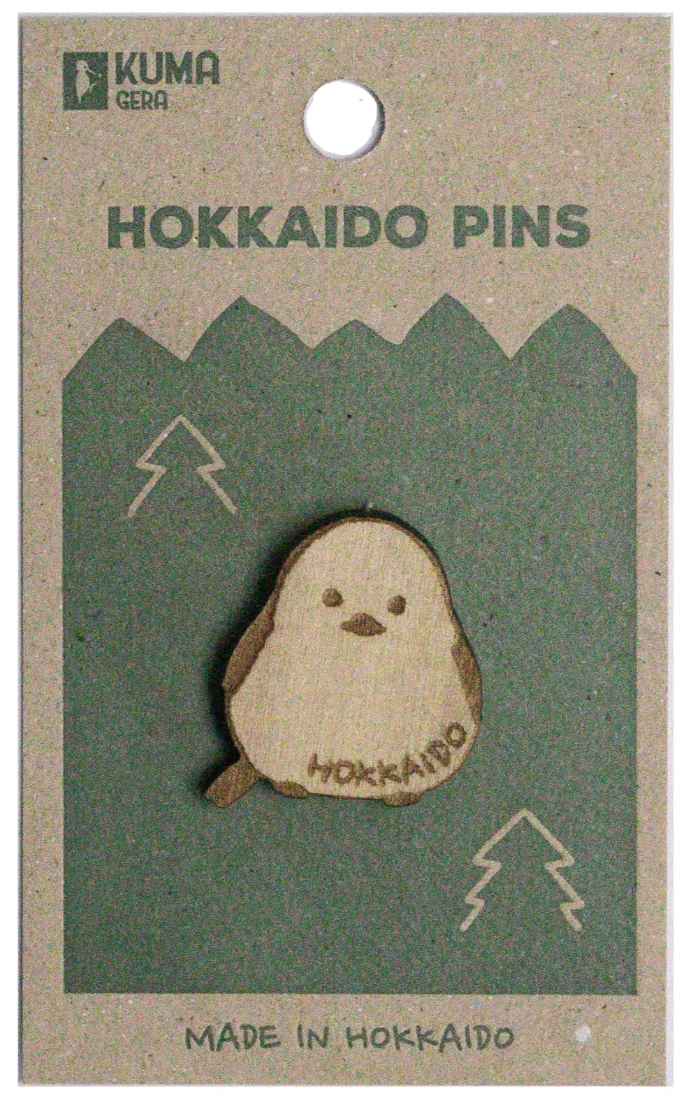 Wooden pin shaped like a cute bird with the word 'HOKKAIDO' engraved on it, on packaging labeled 'Hokkaido Pins' with a mountain and tree graphic, and the text 'Made in Hokkaido'.