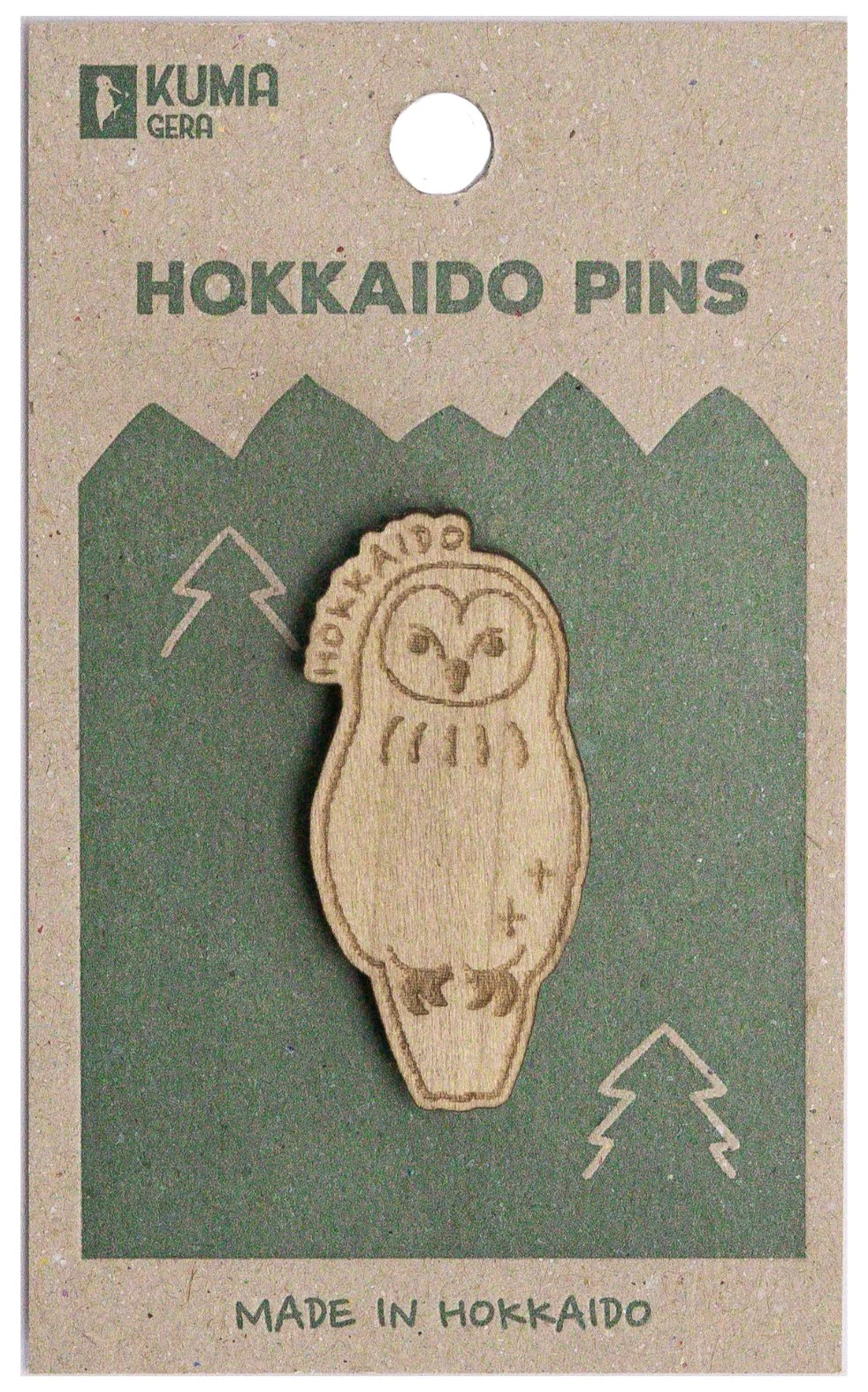 Wooden pin featuring an etched smiling owl with the words 'Hokkaido' on its head, attached to a green and tan cardboard backing labeled 'Hokkaido Pins' and 'Made in Hokkaido'.