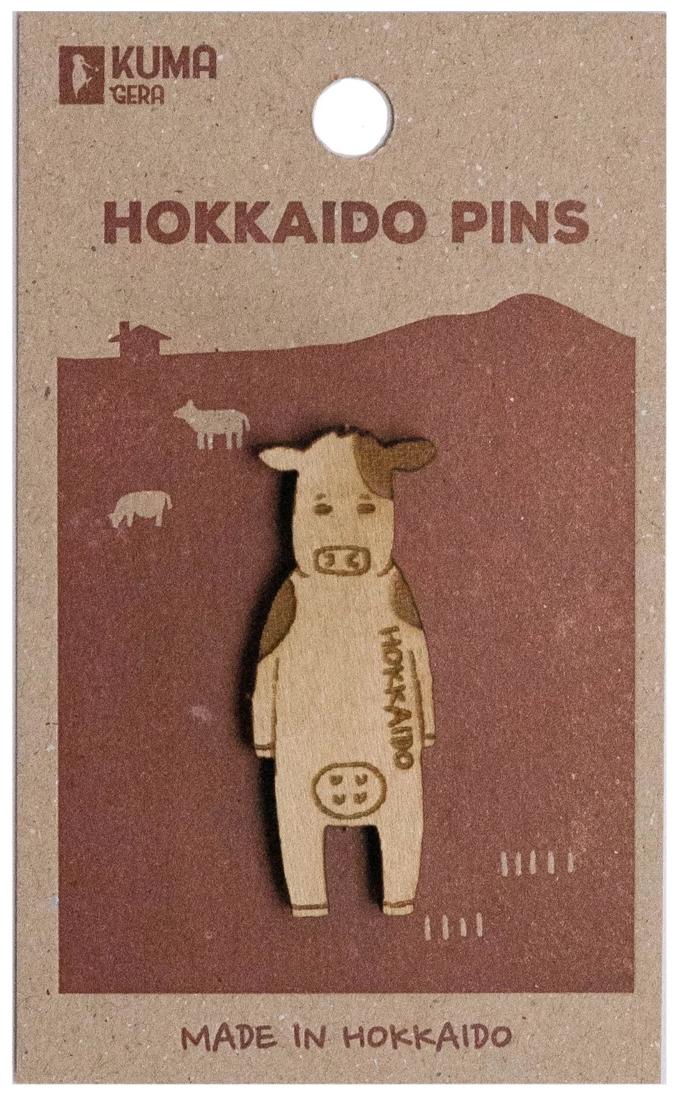 Wooden pin shaped like a cow with 'HOKKAIDO' written on it, on a cardboard backing labeled 'Hokkaido Pins' made in Hokkaido.