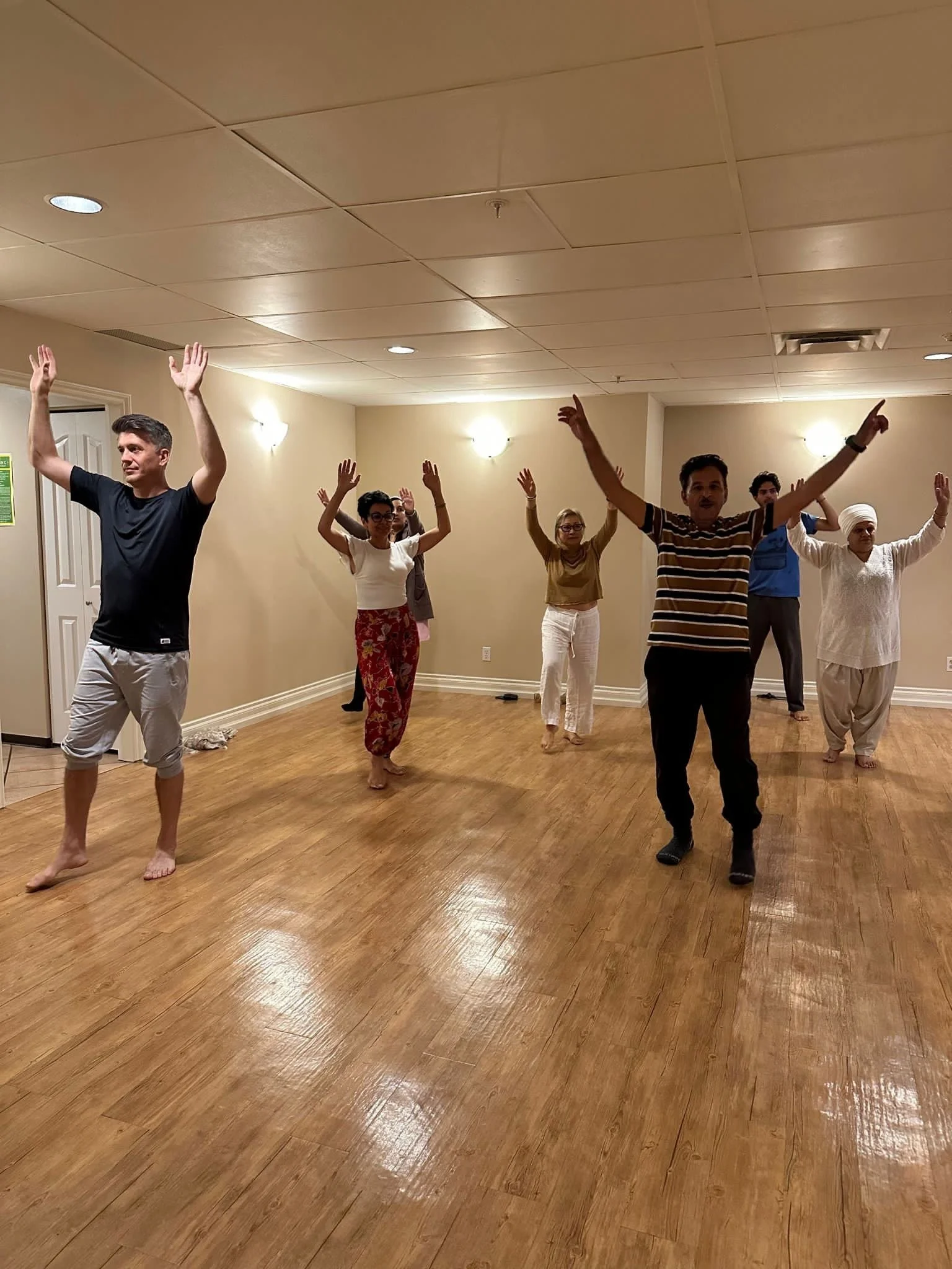People practicing yoga or dance in a spacious, well-lit room with wooden floors.