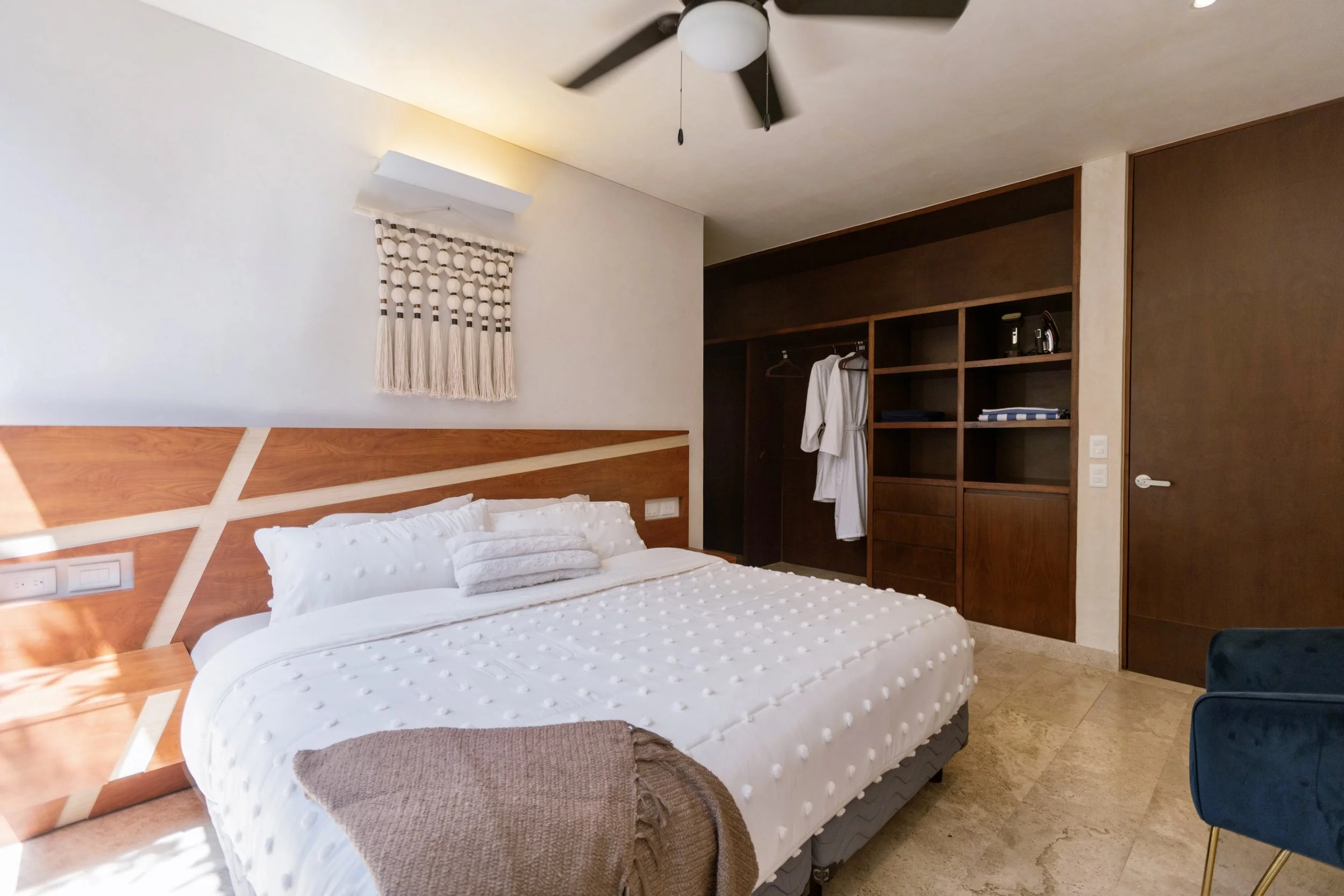 Hotel room with a bed, wooden headboard, and built-in wardrobe, with a white robe hanging inside