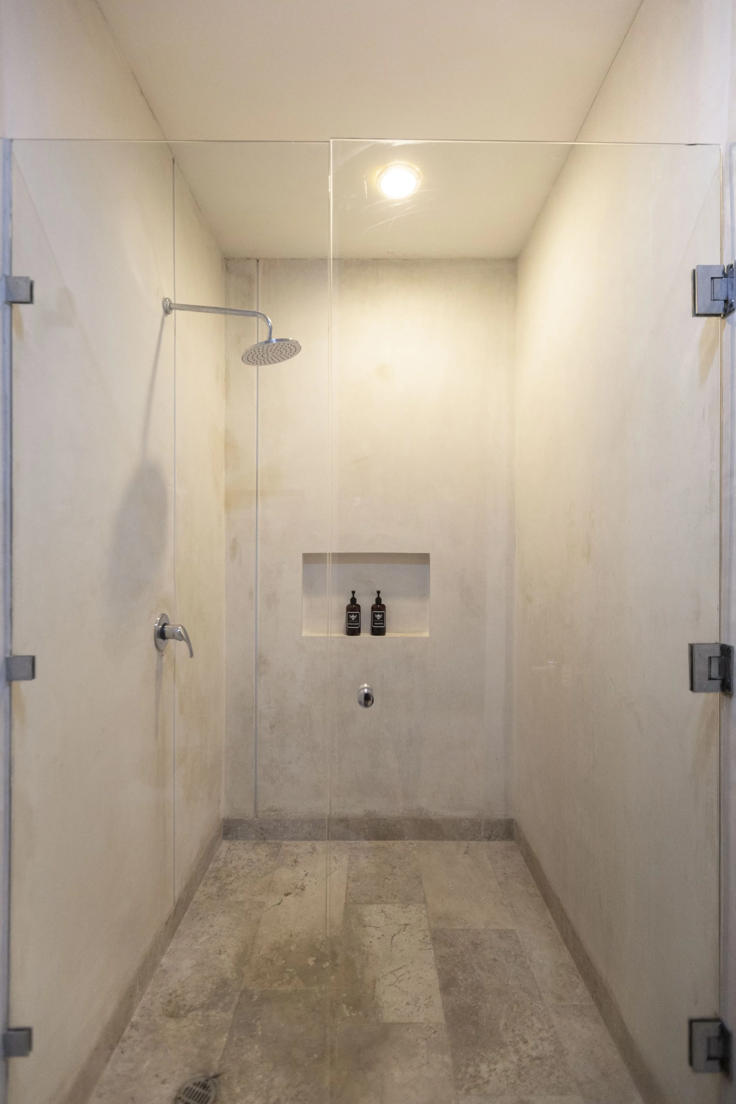 Empty shower with a rain showerhead, a built-in shelf with two bottles, and a drain on the tiled floor.