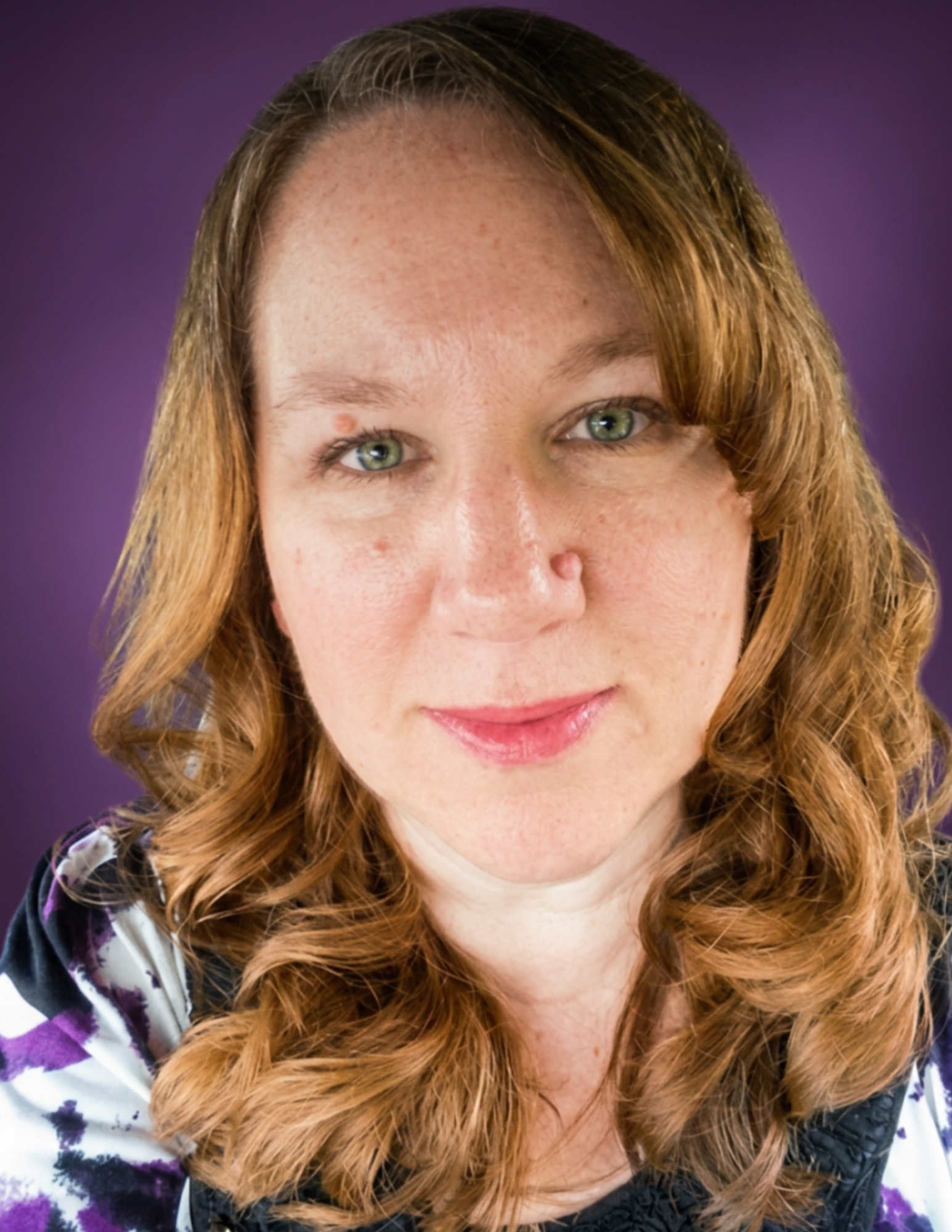 A close-up of a woman with long, curly red hair and green eyes, smiling slightly, with a purple gradient background.