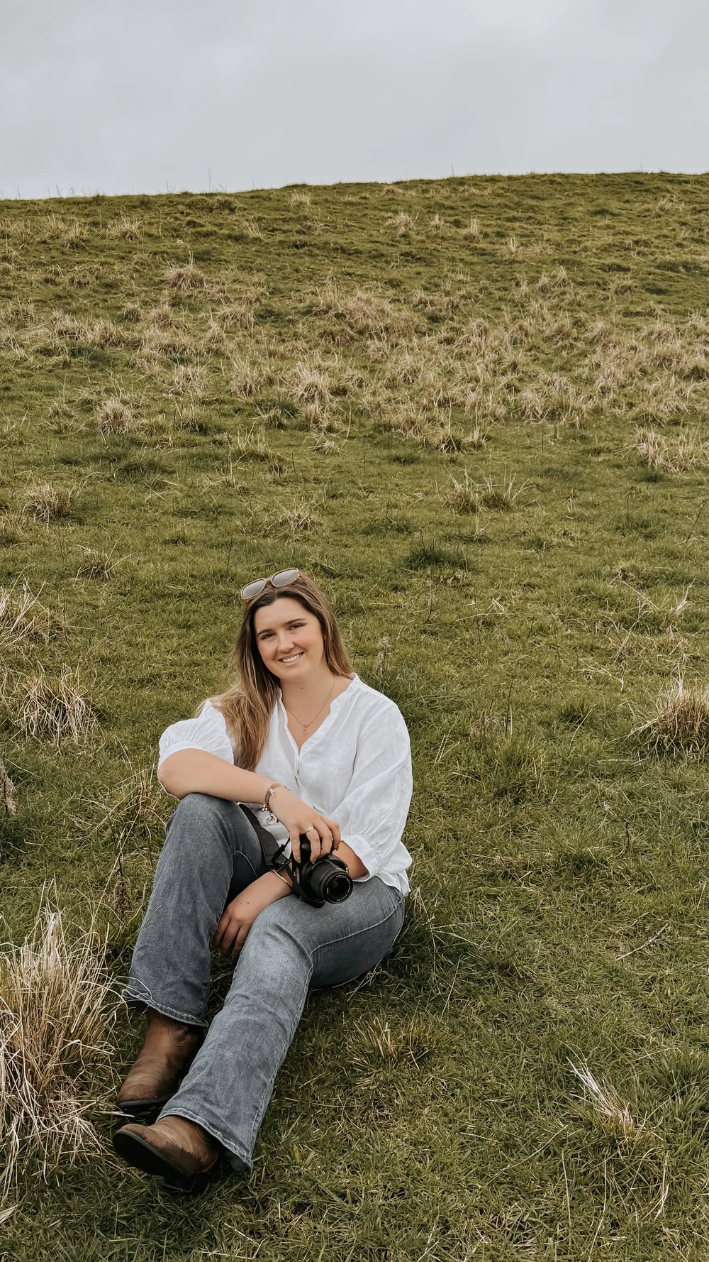 Rosie sitting on a hillside holding a camera and smiling