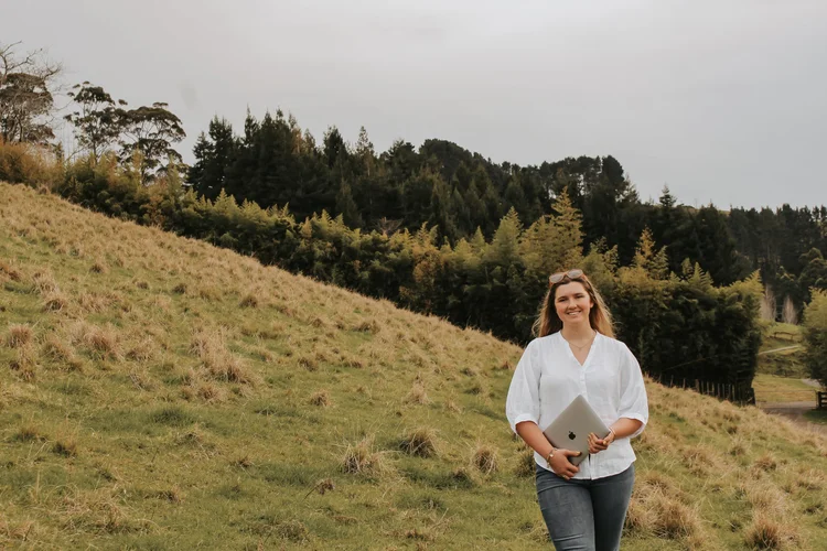 Rosie walking on a grassy hillside holding a laptop