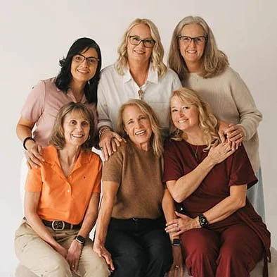 six smiling women standing in front of a plain backdrop