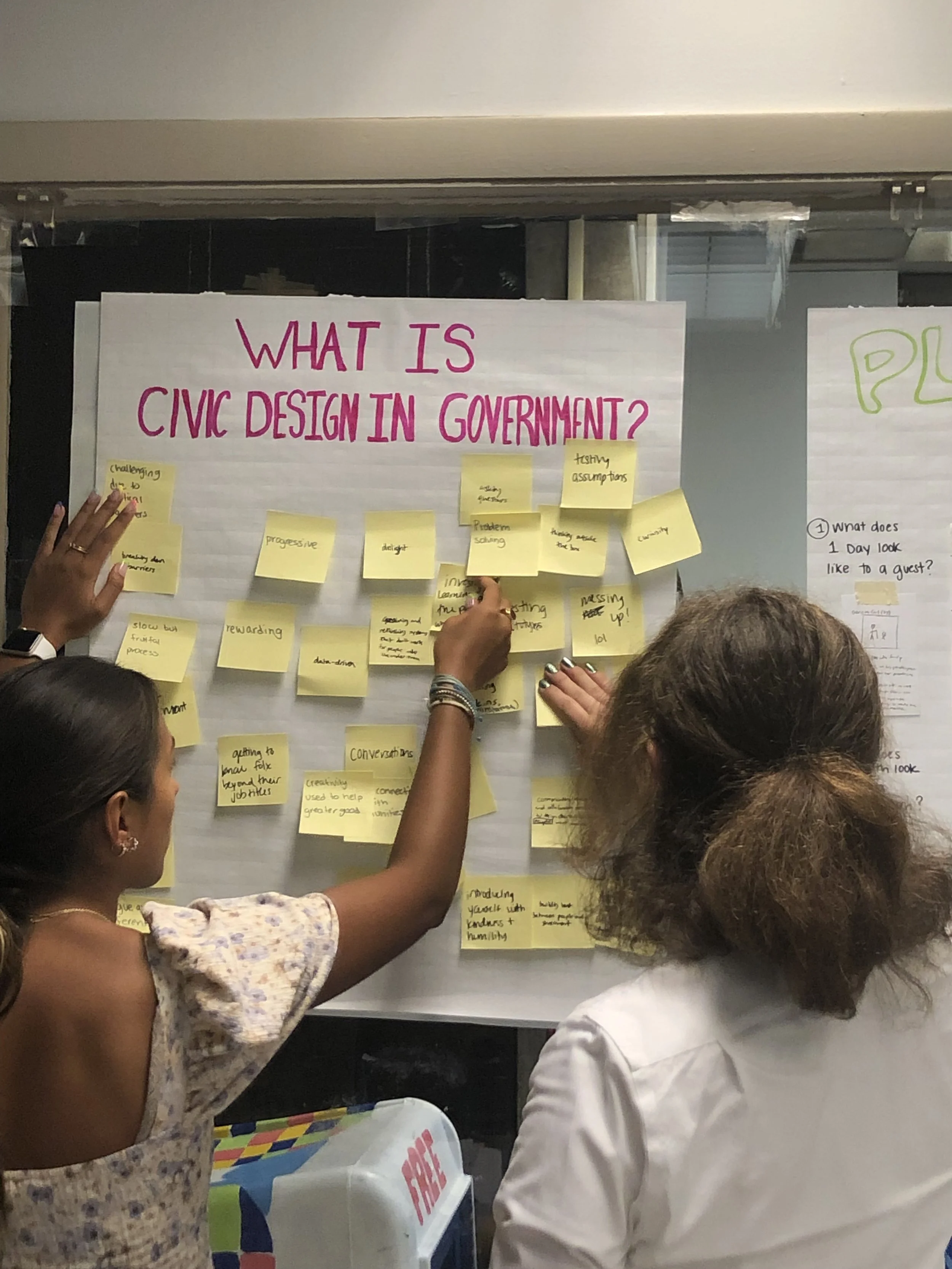 two young people hold post-it notes up to a poster that says, "what is civic design in government?"