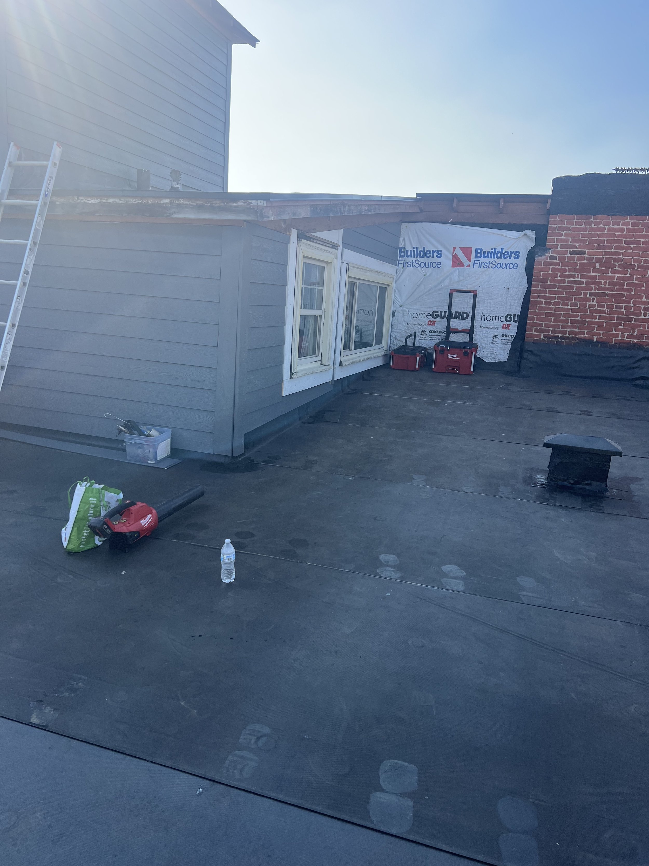 Rooftop construction site with a partially built wall, stacked tools, a water bottle, and construction materials.