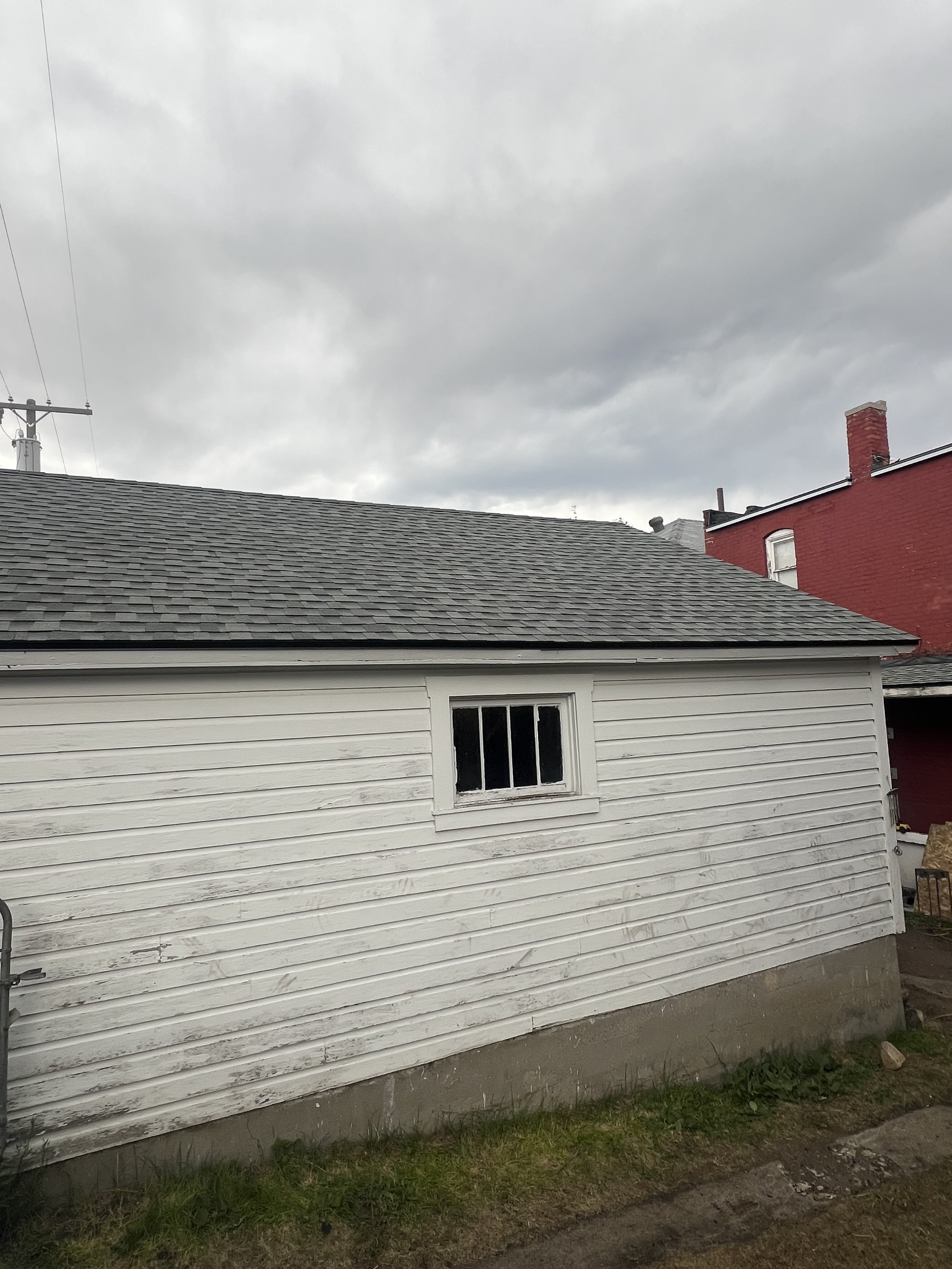 White wooden house with a small window, gray shingle roof, and cloudy sky overhead.