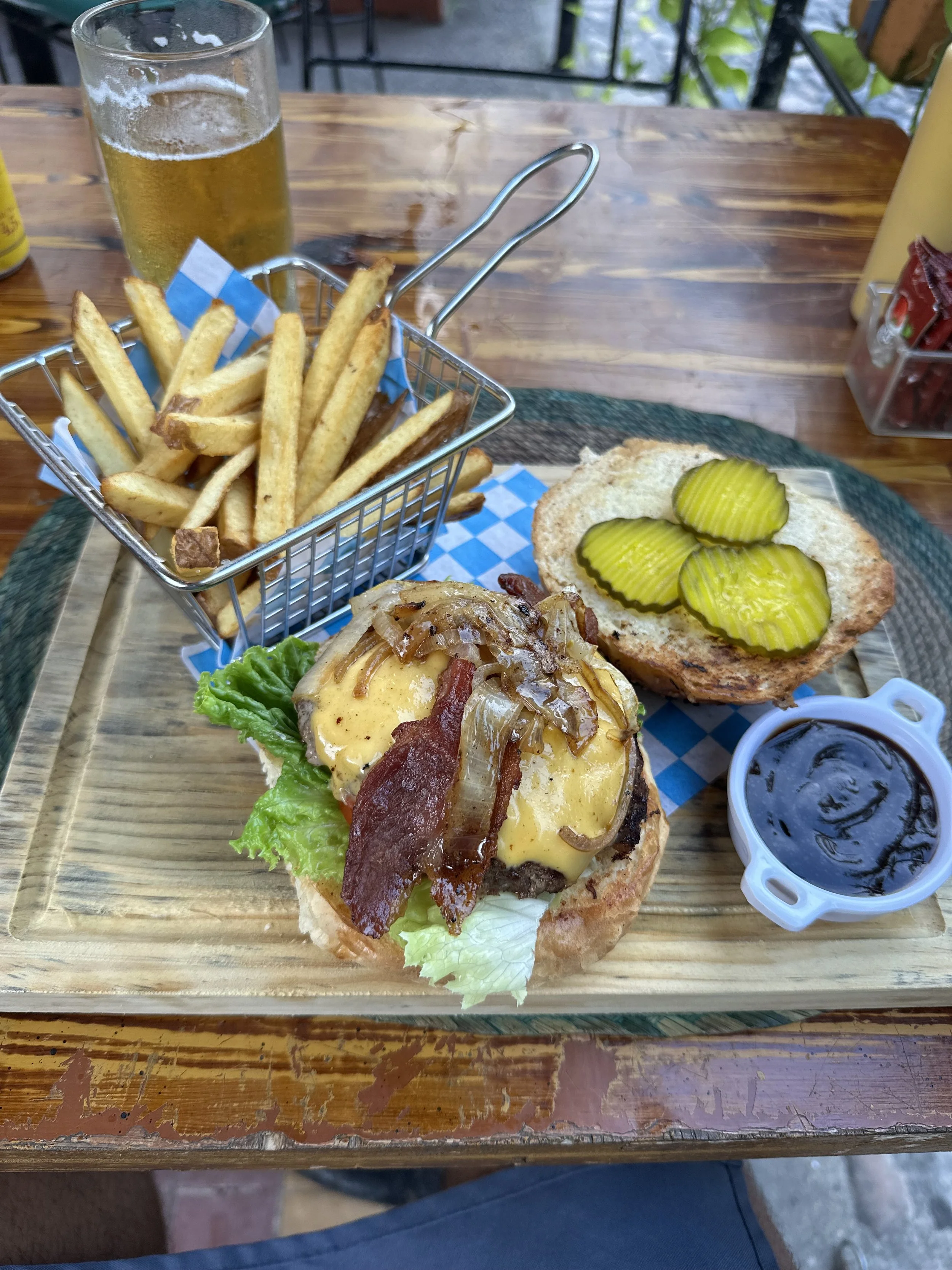 A burger and fries on a wood table in Mexico accompanied by a beer