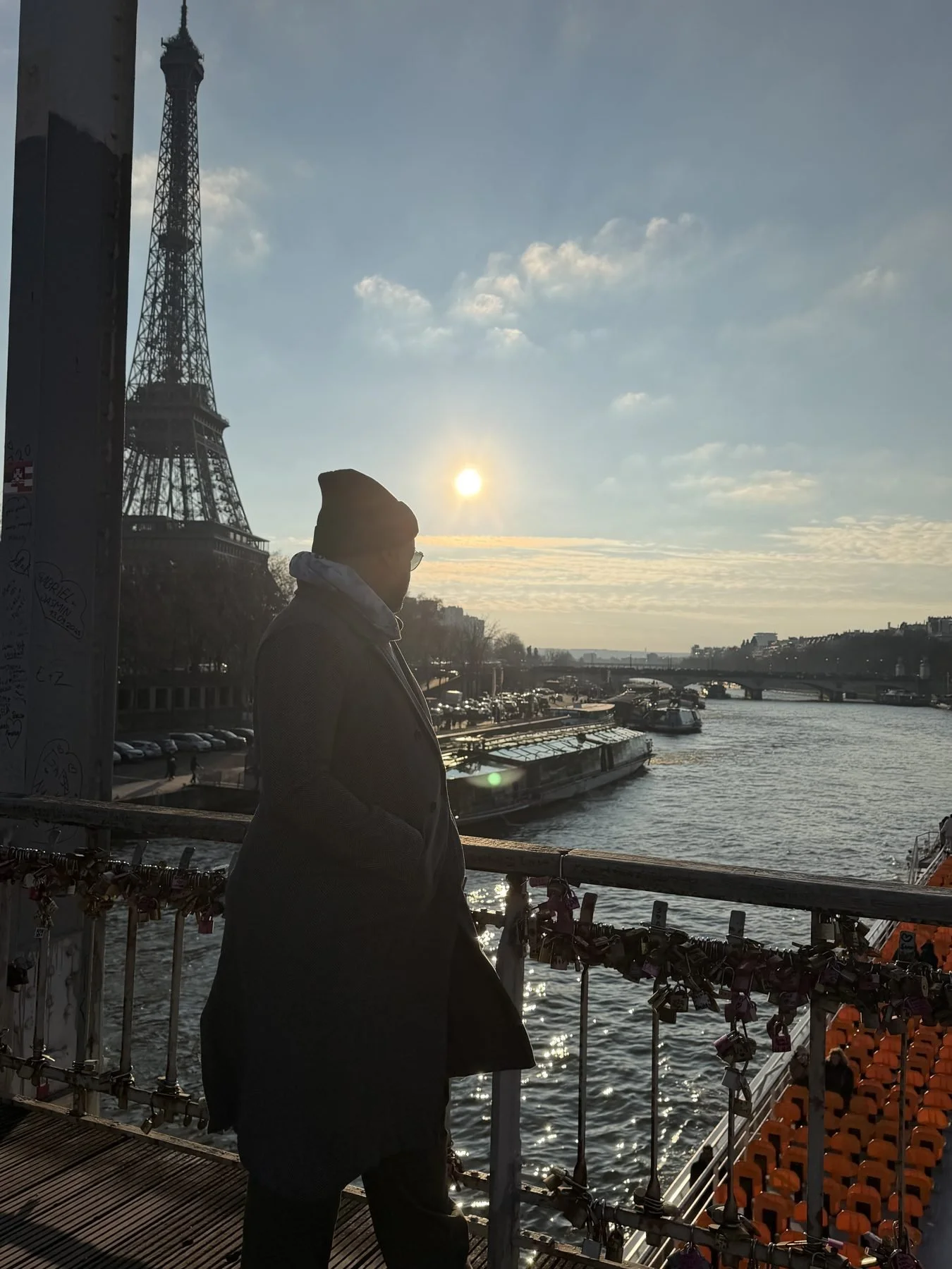 Nick in a long coat on a bridge over the Seine with the Eiffel Tower behind him at Christmas