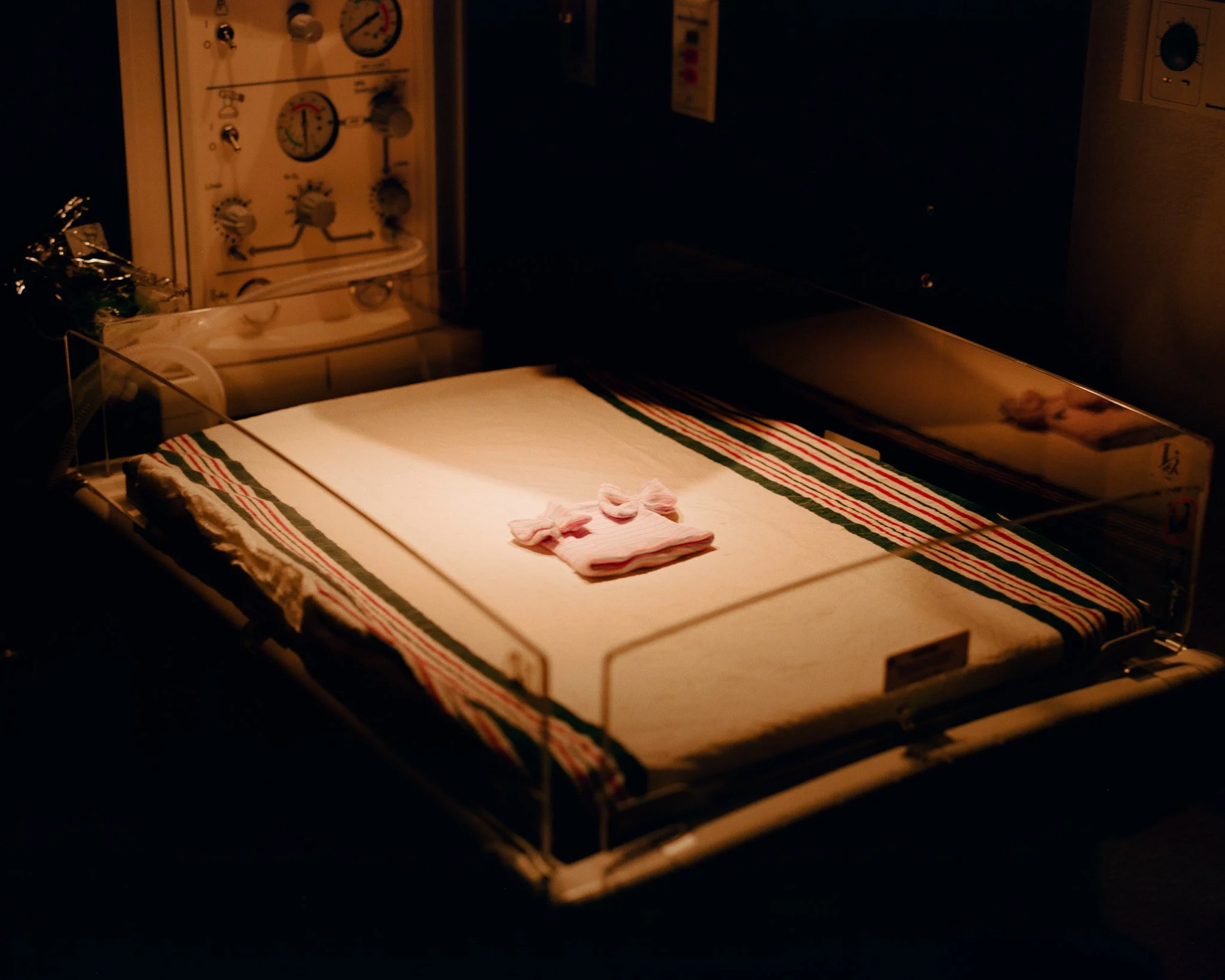 A neonatal incubator with a set of tiny pink socks inside, illuminated by soft light.