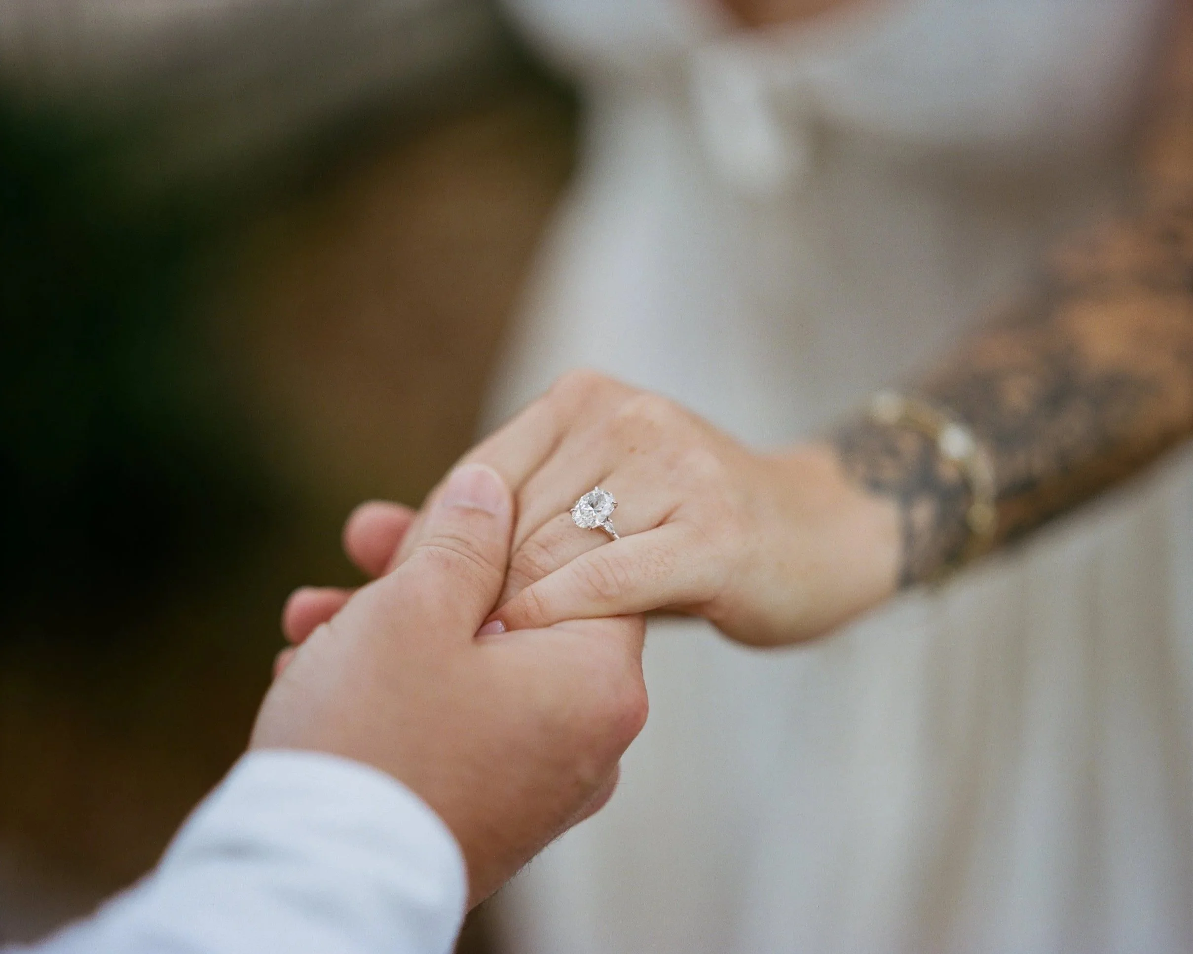Close-up of a woman wearing a yellow floral dress, gold necklace with a square pendant, and sunglasses, with her hand near her head, outdoors during daytime.