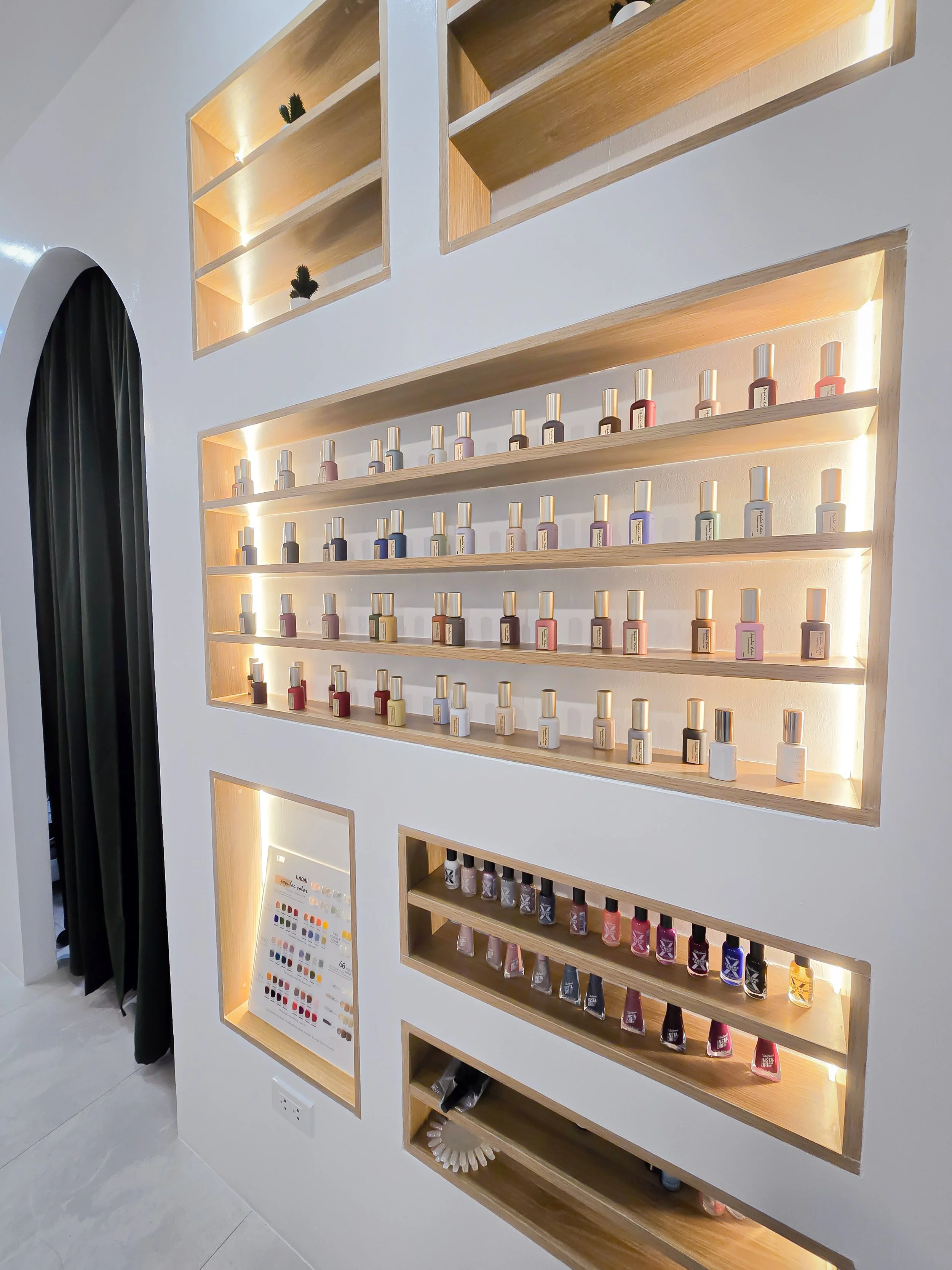 Display of nail polish bottles arranged on wooden shelves with built-in lighting in a modern shop interior.