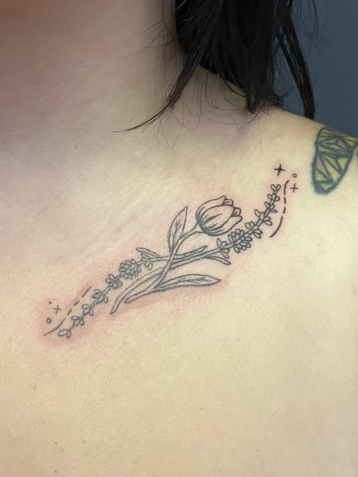 Tattoo of a flower, a tulip, with leaves and stems, with small decorative elements and dashed lines added around it.