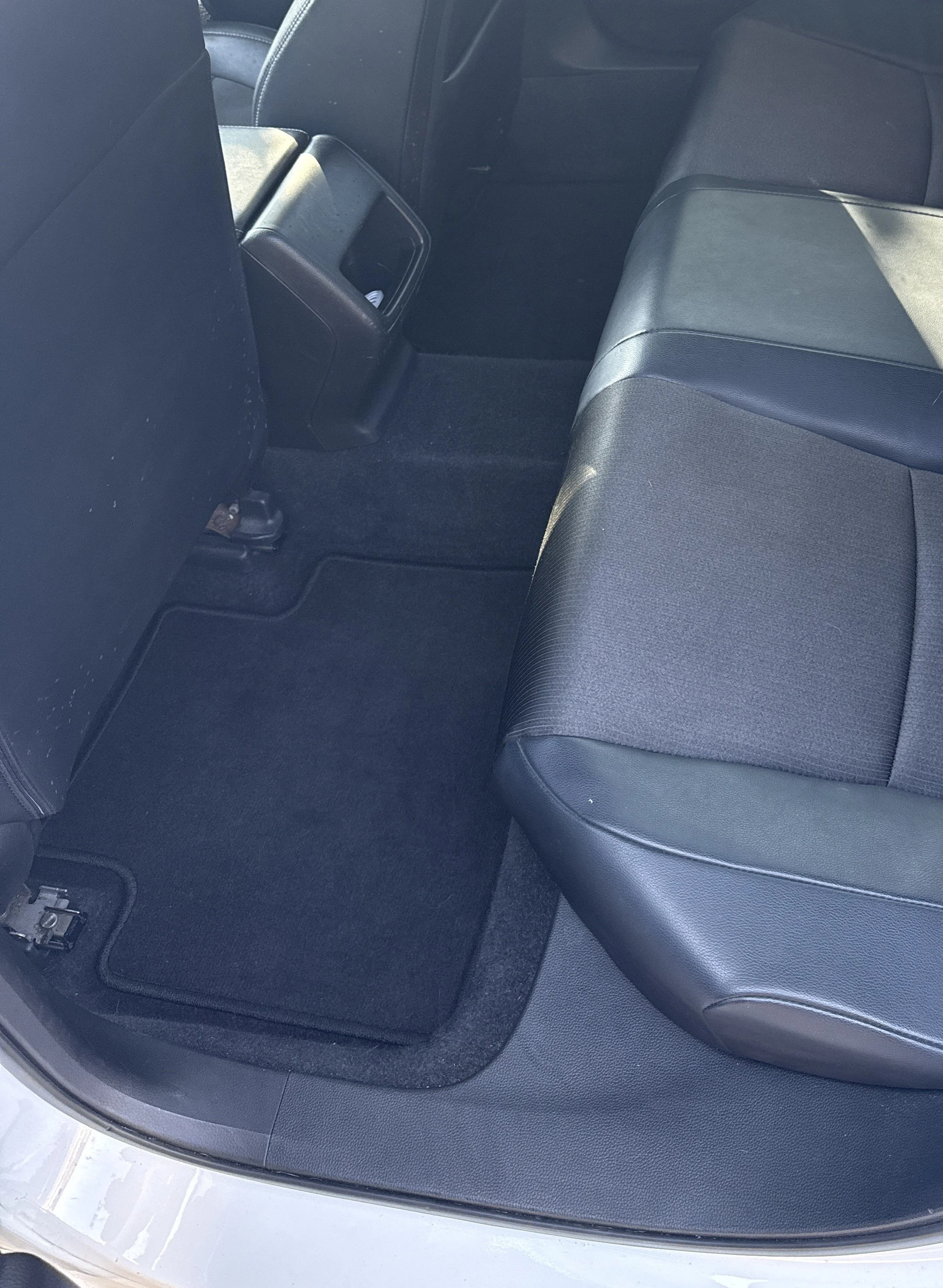 Back seat area of a car with black fabric and leather seats, showing the floor and part of the rear door frame.