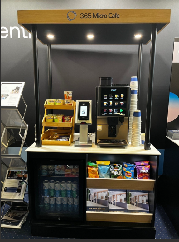 Koffie- en snackbarstandaard met koffiezetapparaat, snacks, bekers en drankjes.