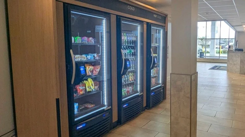 Vijf vendingmachines in een lobby, gevuld met snacks en drankjes.