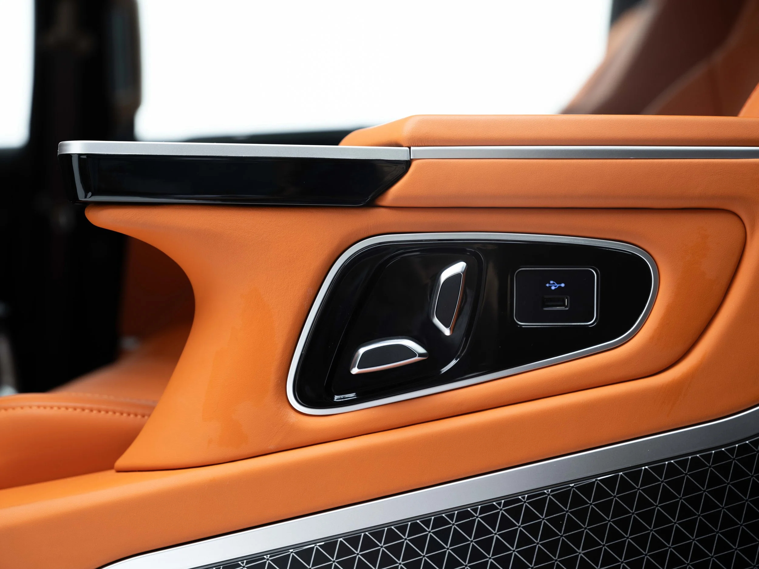 Close-up of a car's interior door panel with seat adjustment controls, USB port, and orange leather upholstery.