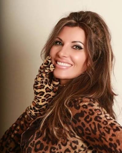 A woman with long, wavy brunette hair smiling and wearing a leopard print top and glove.